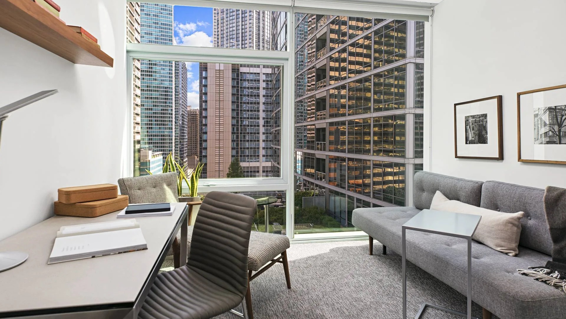 Bright home office with desk, sofa, and floor-to-ceiling windows overlooking downtown Chicago at Optima Signature apartments