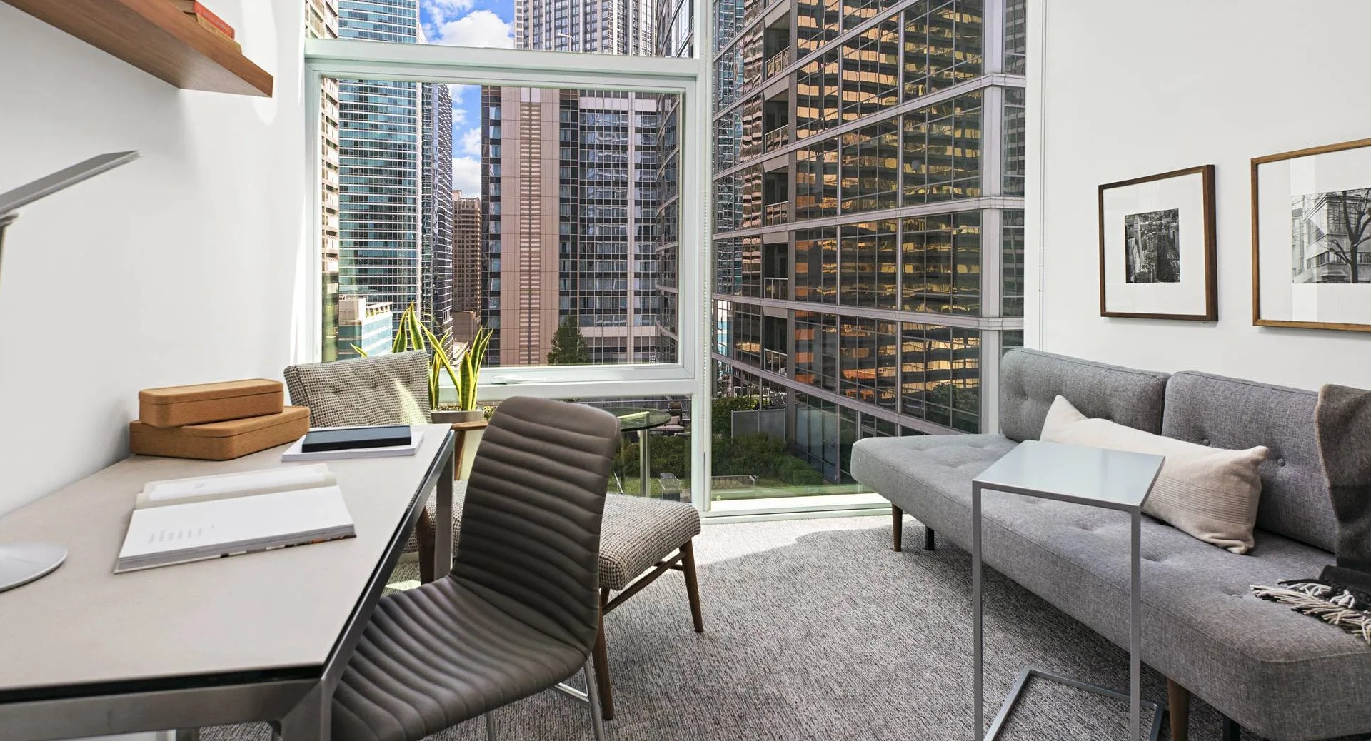 Bright home office with desk, sofa, and floor-to-ceiling windows overlooking downtown Chicago at Optima Signature apartments