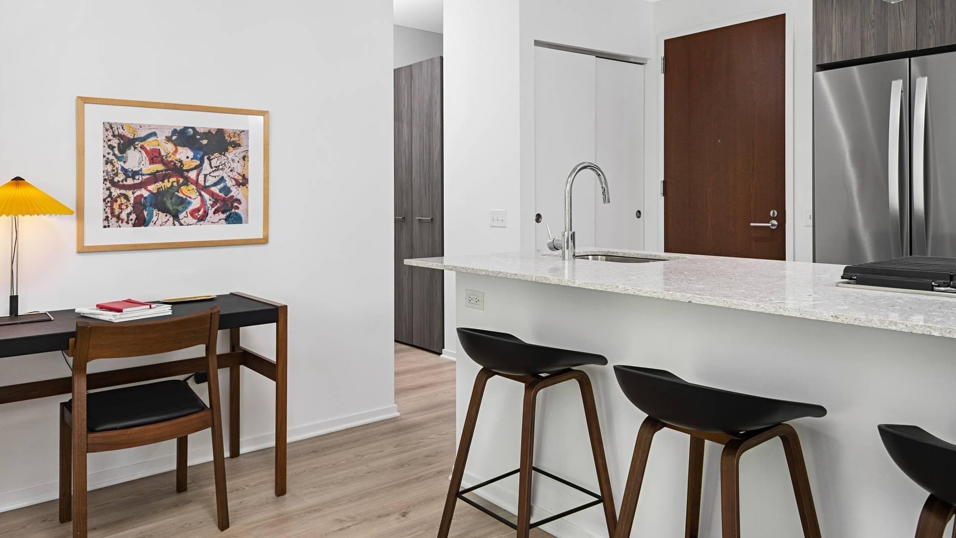 Kitchen at Optima Signature with granite island and stainless appliances, alongside a small desk workspace with modern lighting