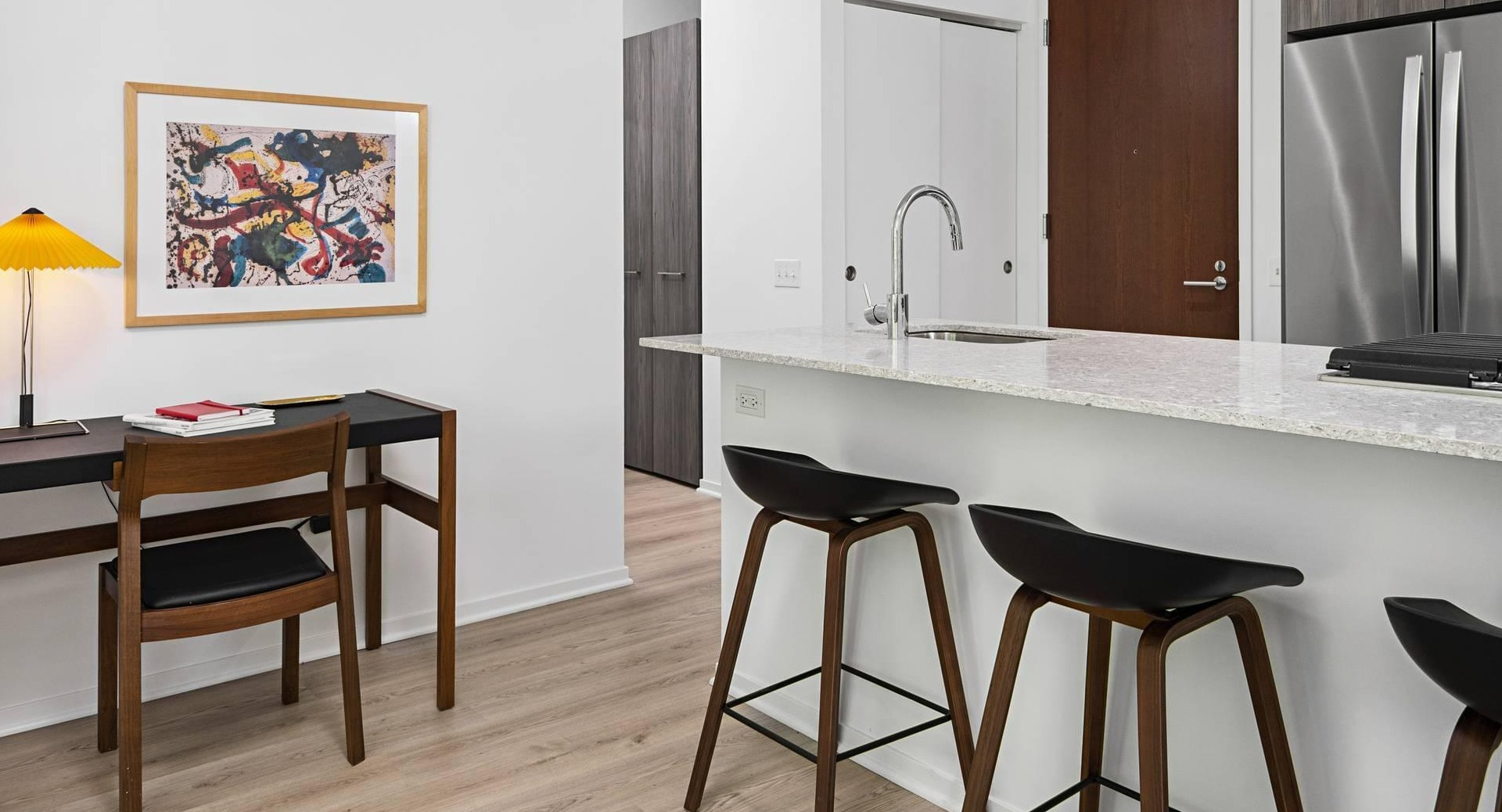 Kitchen at Optima Signature with granite island and stainless appliances, alongside a small desk workspace with modern lighting