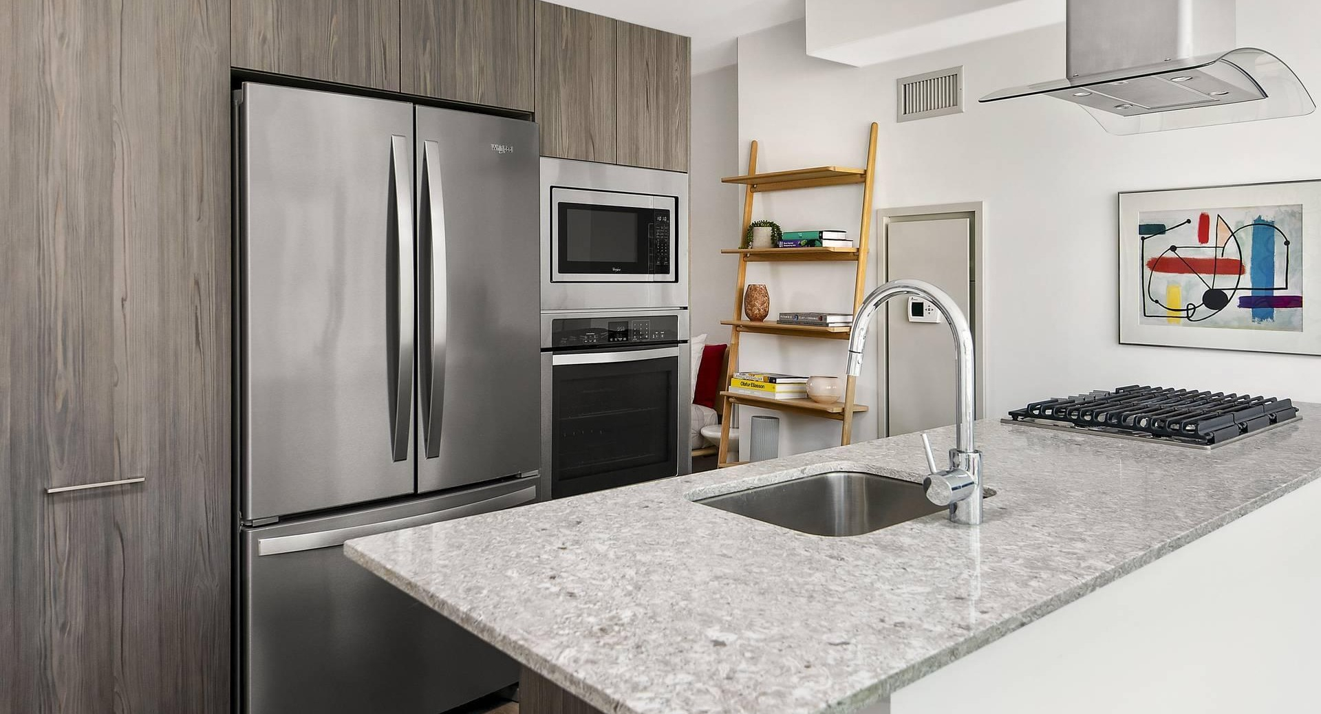 Open kitchen layout at Optima Signature with granite counters, stainless steel fridge, and wood cabinetry
