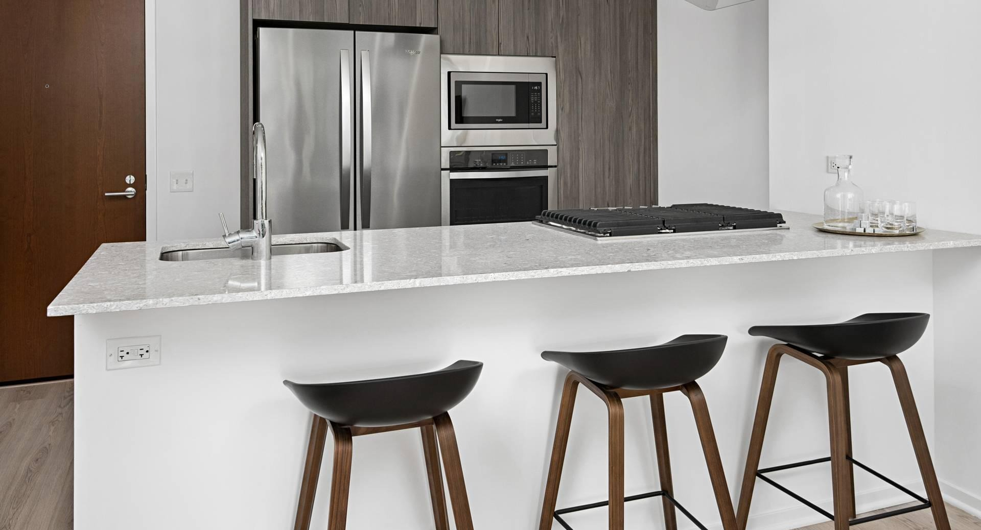 Modern kitchen at Optima Signature with sleek cabinetry, stainless steel appliances, and a breakfast bar with seating