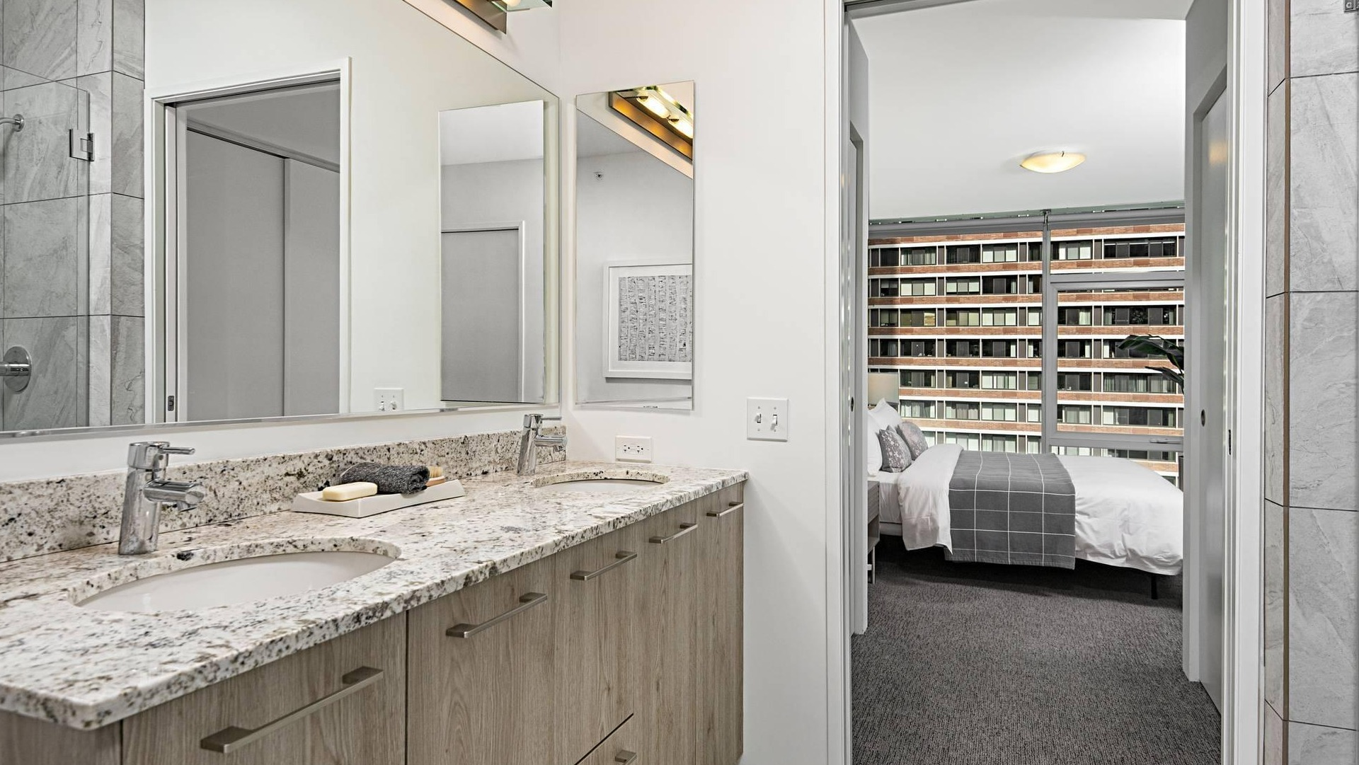 Primary bathroom at Optima Signature featuring double vanities, separate glass shower, and bedroom access for convenient ensuite living