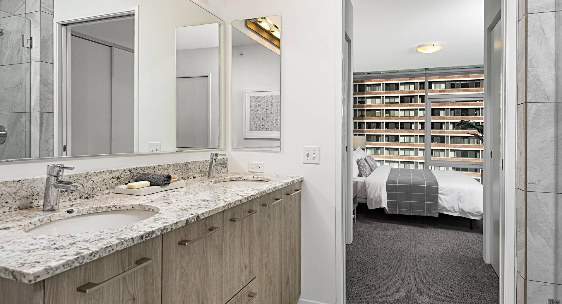 Primary bathroom at Optima Signature featuring double vanities, separate glass shower, and bedroom access for convenient ensuite living