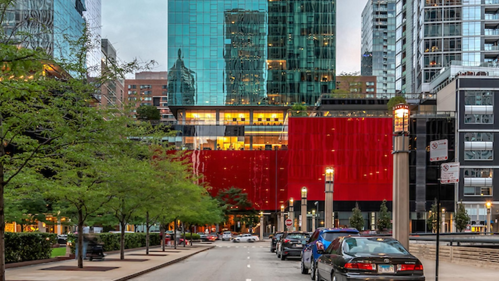 Street view of Optima Signature’s striking glass tower with red podium, framed by neighboring high-rises in downtown Chicago