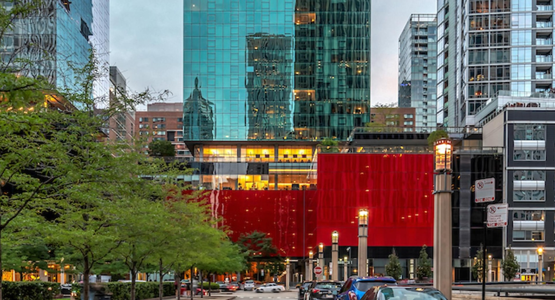 Street view of Optima Signature’s striking glass tower with red podium, framed by neighboring high-rises in downtown Chicago