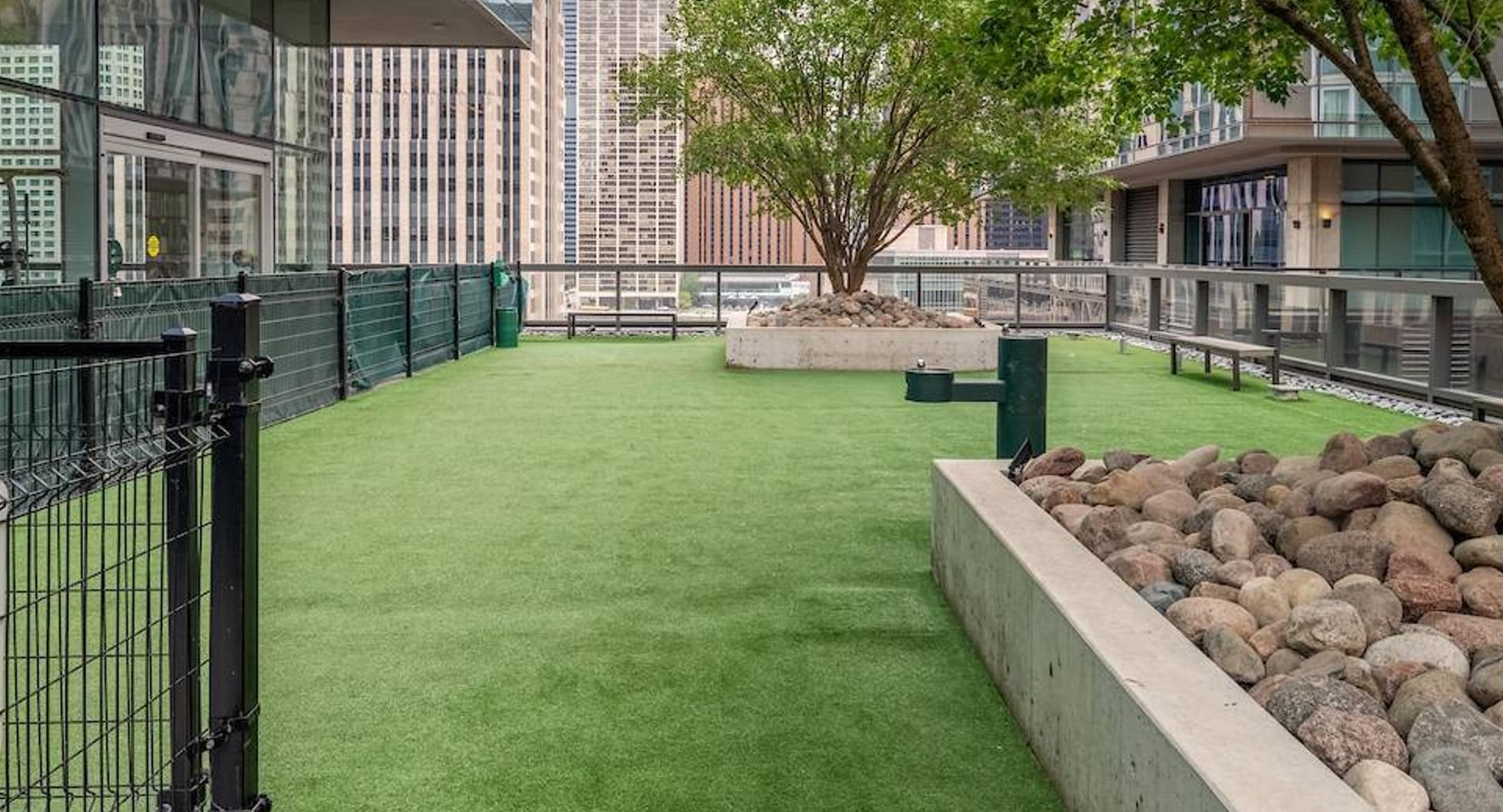 Outdoor dog park with fenced green turf, trees, and city views designed for residents at Optima Signature apartments in Chicago