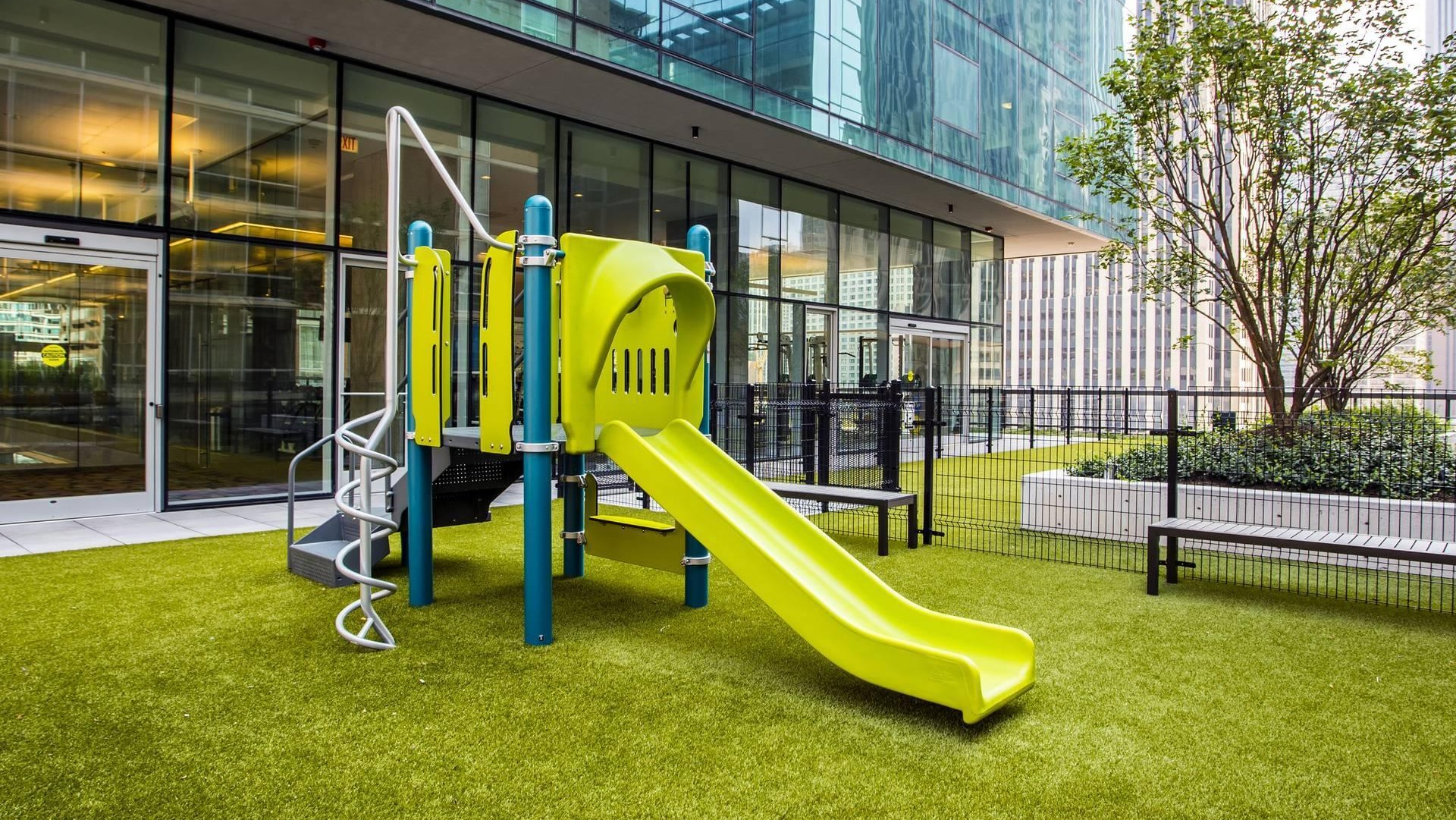 Outdoor playground with bright green slide, climbing features, and safe turf play area at Optima Signature apartments in Chicago