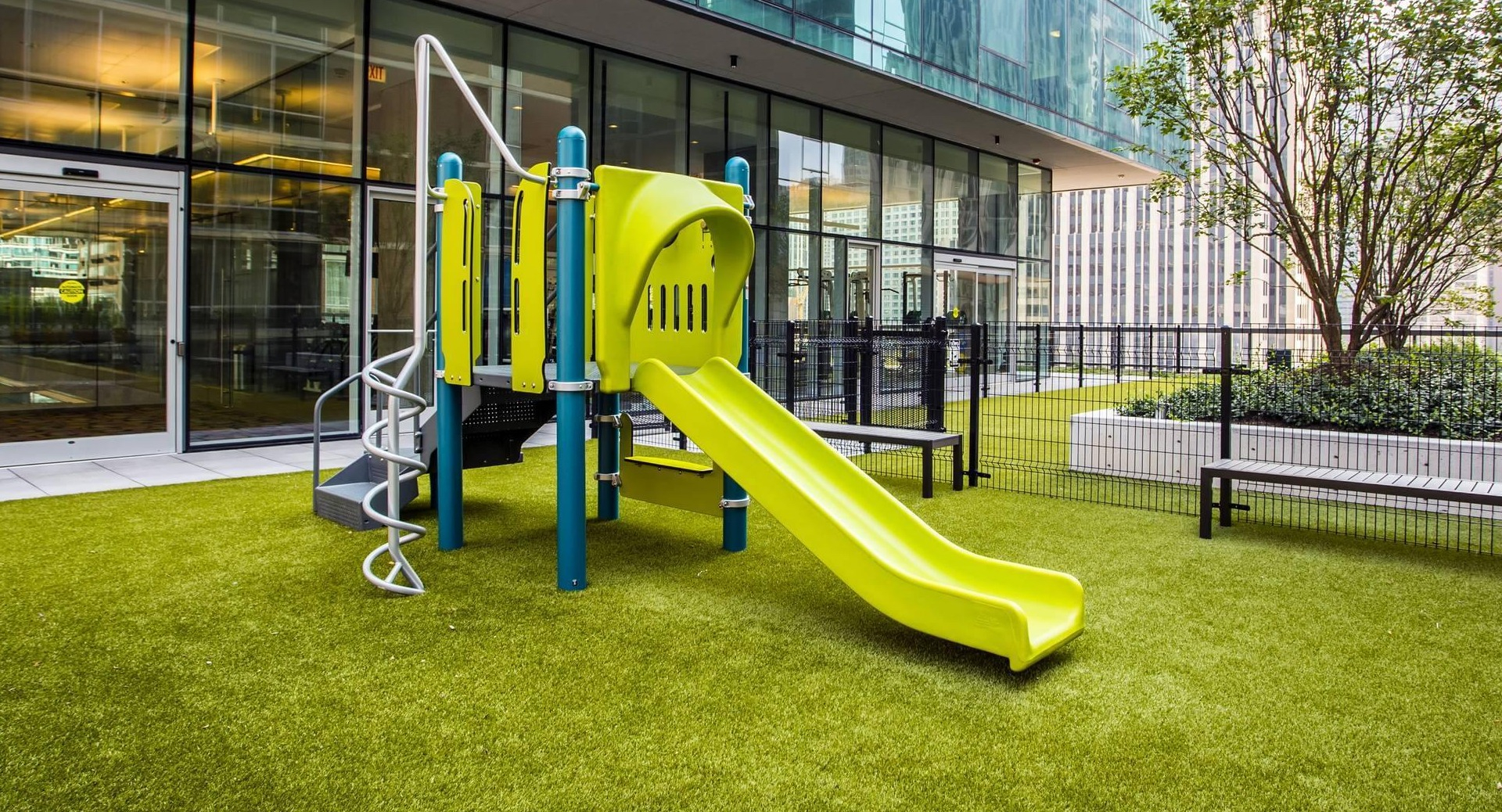 Outdoor playground with bright green slide, climbing features, and safe turf play area at Optima Signature apartments in Chicago