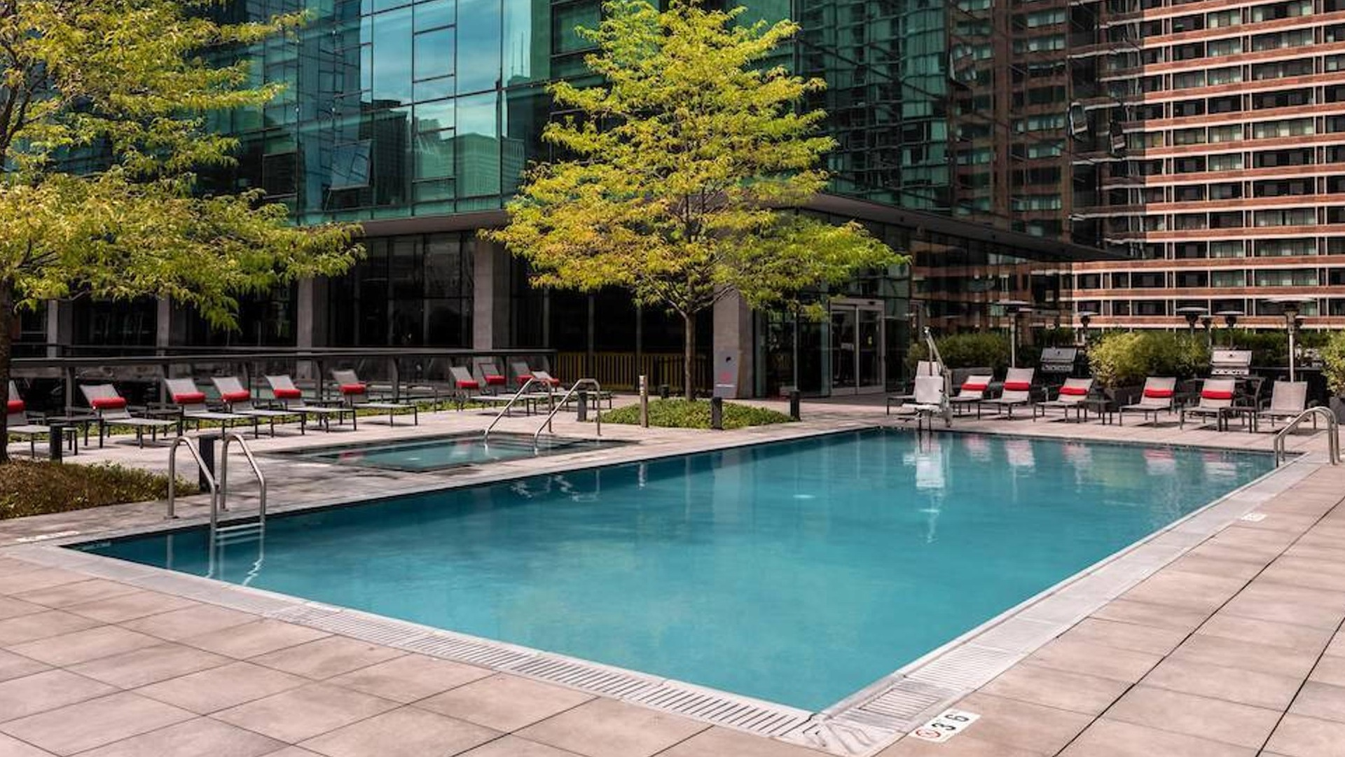 Outdoor pool framed by modern glass towers with lounge seating and landscaped deck at Optima Signature apartments in Chicago