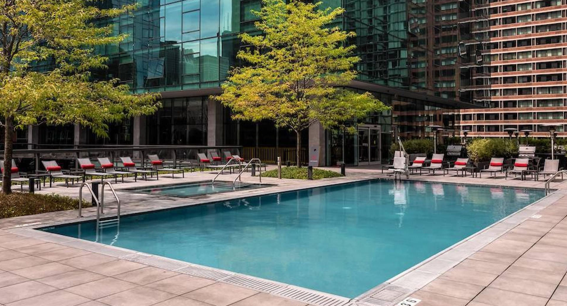 Outdoor pool framed by modern glass towers with lounge seating and landscaped deck at Optima Signature apartments in Chicago