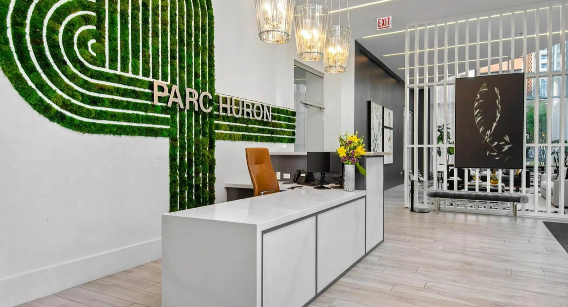 Vibrant lobby reception at Parc Huron in Chicago, featuring a modern desk, a unique moss green wall art, and elegant lighting
