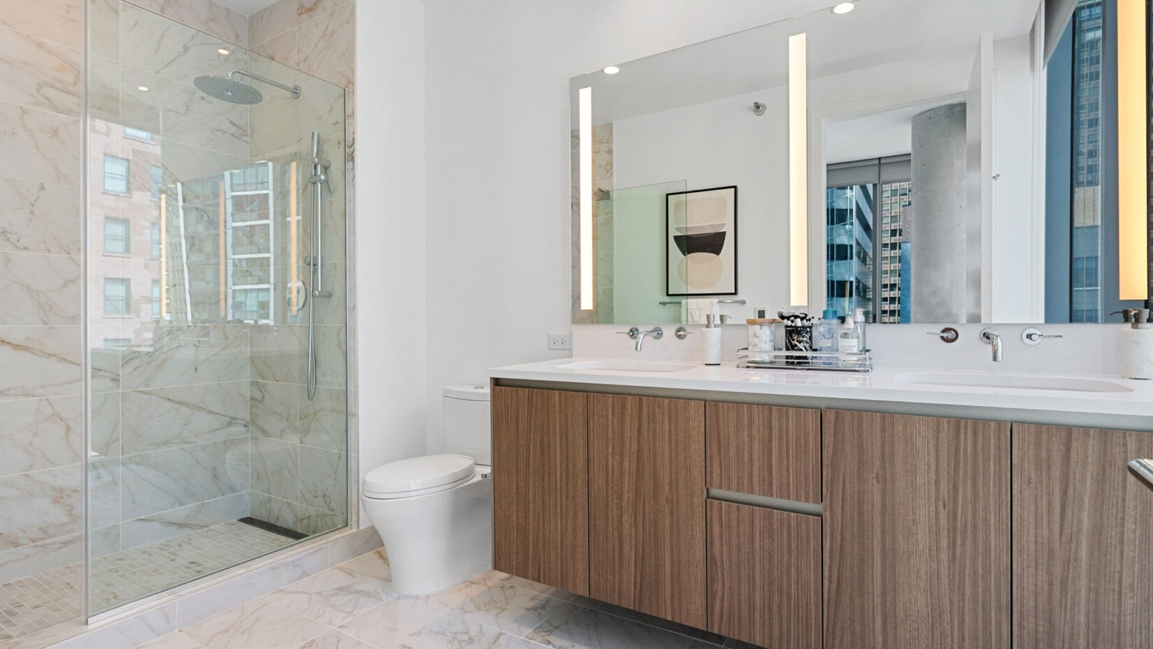 Luxurious bathroom with a double wood vanity, marble shower, and illuminated mirrors at Parkline Chicago in Chicago
