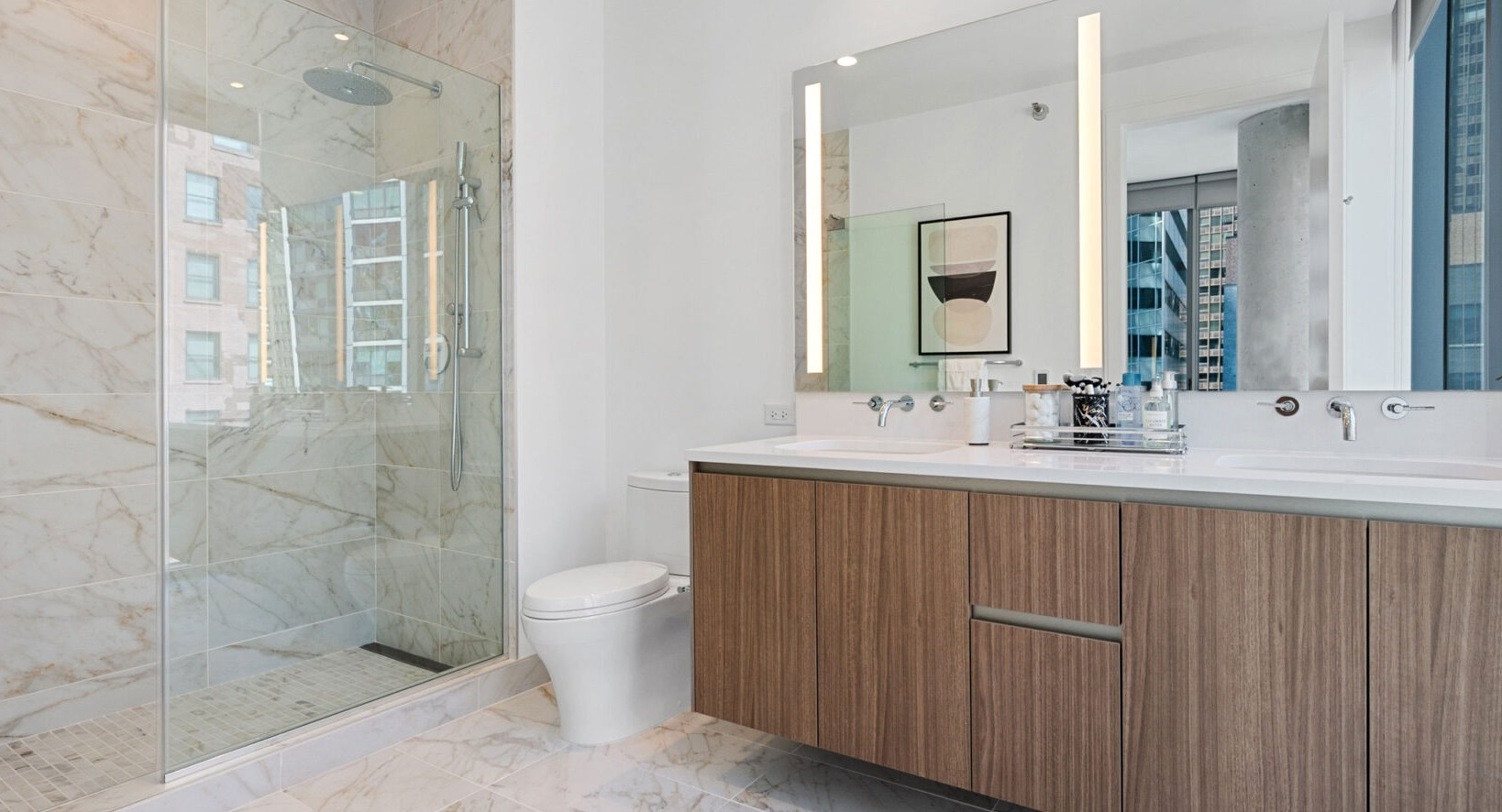 Luxurious bathroom with a double wood vanity, marble shower, and illuminated mirrors at Parkline Chicago in Chicago