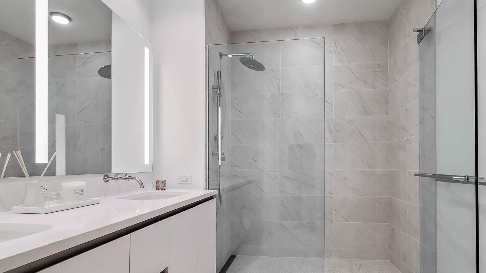 Modern bathroom with a double vanity, large illuminated mirror, and a spacious walk-in shower at Parkline Chicago in Chicago