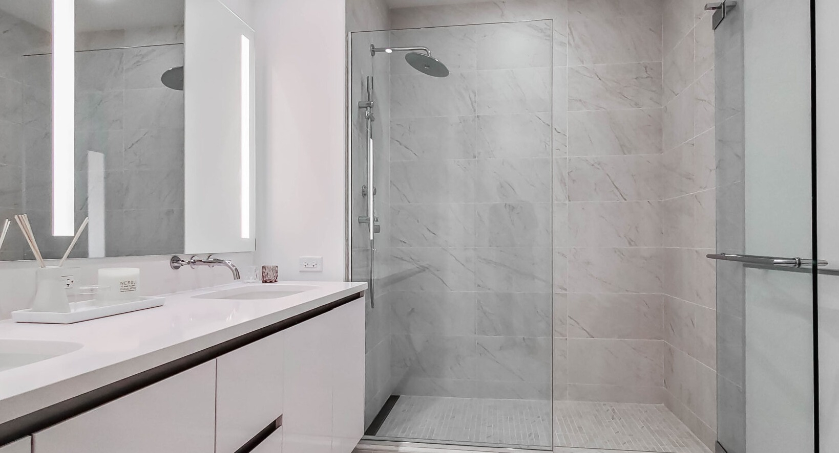 Modern bathroom with a double vanity, large illuminated mirror, and a spacious walk-in shower at Parkline Chicago in Chicago