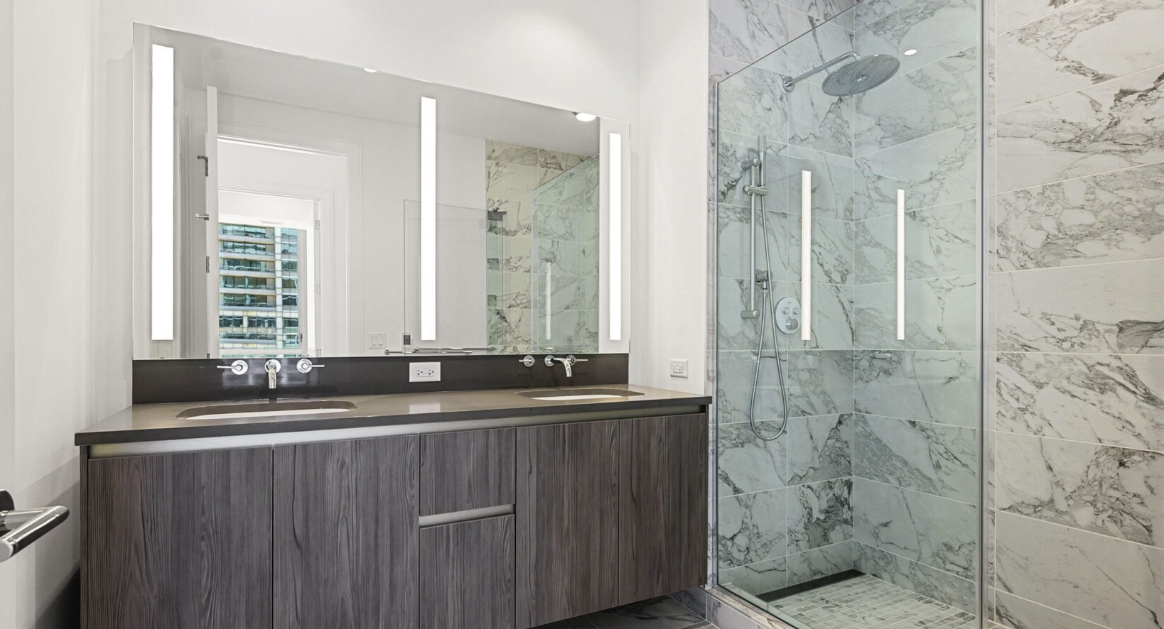 Luxurious bathroom with a double vanity, modern fixtures, and a spacious walk-in shower with marble tiling at Parkline Chicago in Chicago