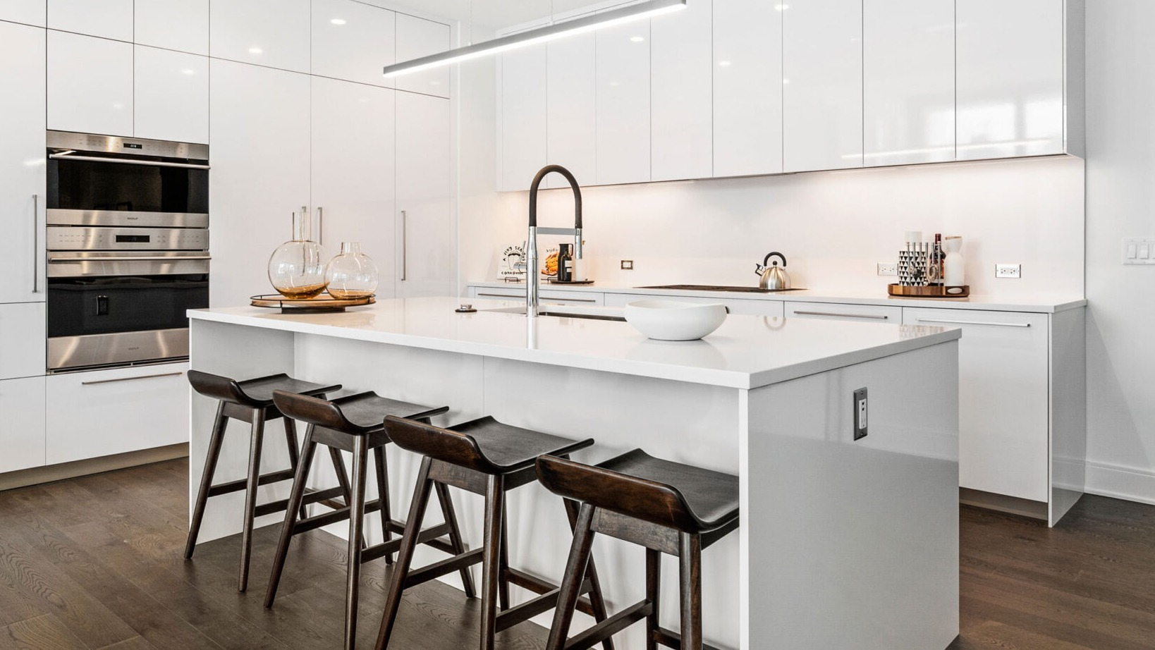 Sleek white kitchen with a large island, modern bar stools, integrated appliances, and pendant lighting at Parkline Chicago in Chicago