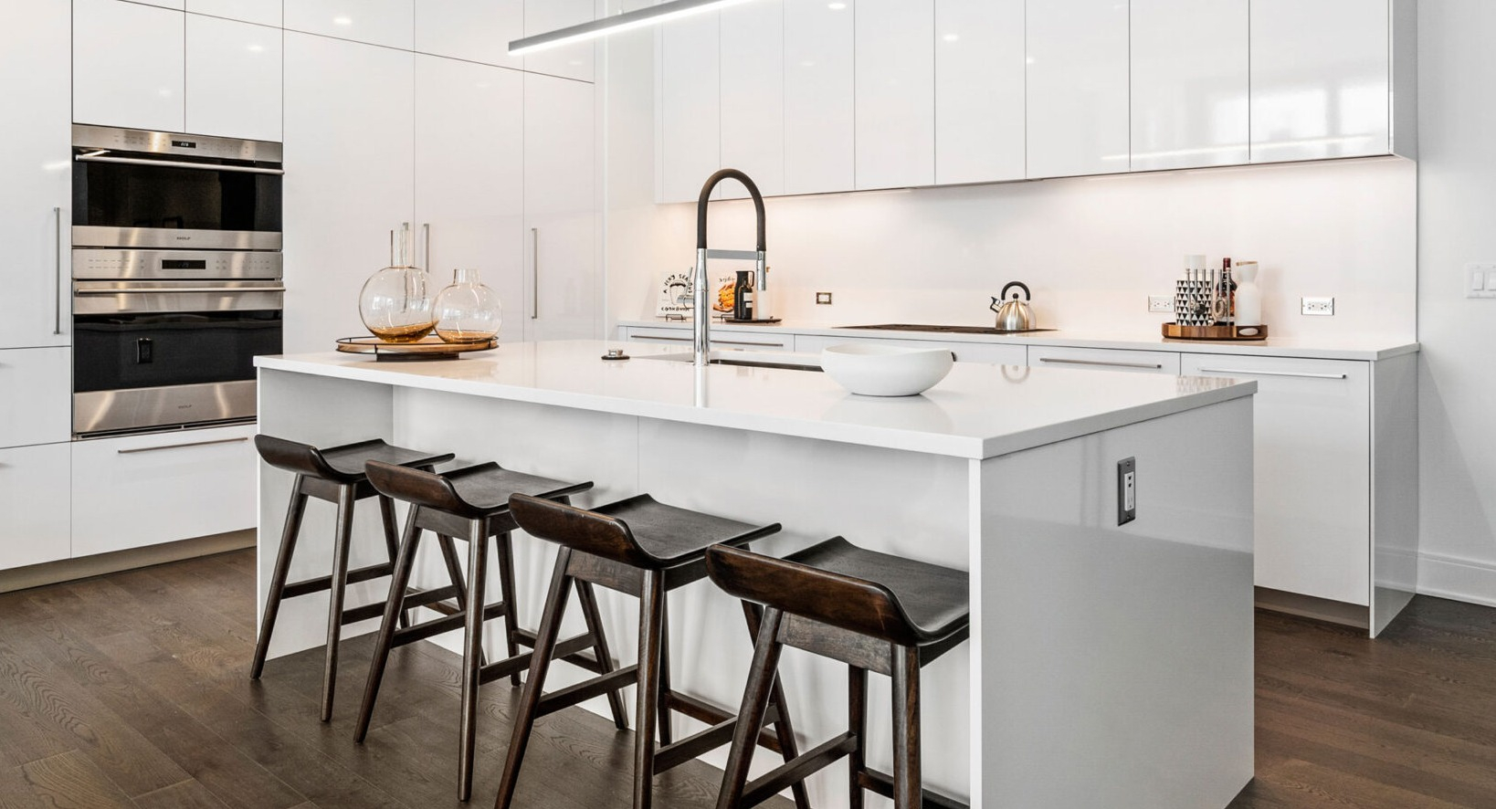 Sleek white kitchen with a large island, modern bar stools, integrated appliances, and pendant lighting at Parkline Chicago in Chicago