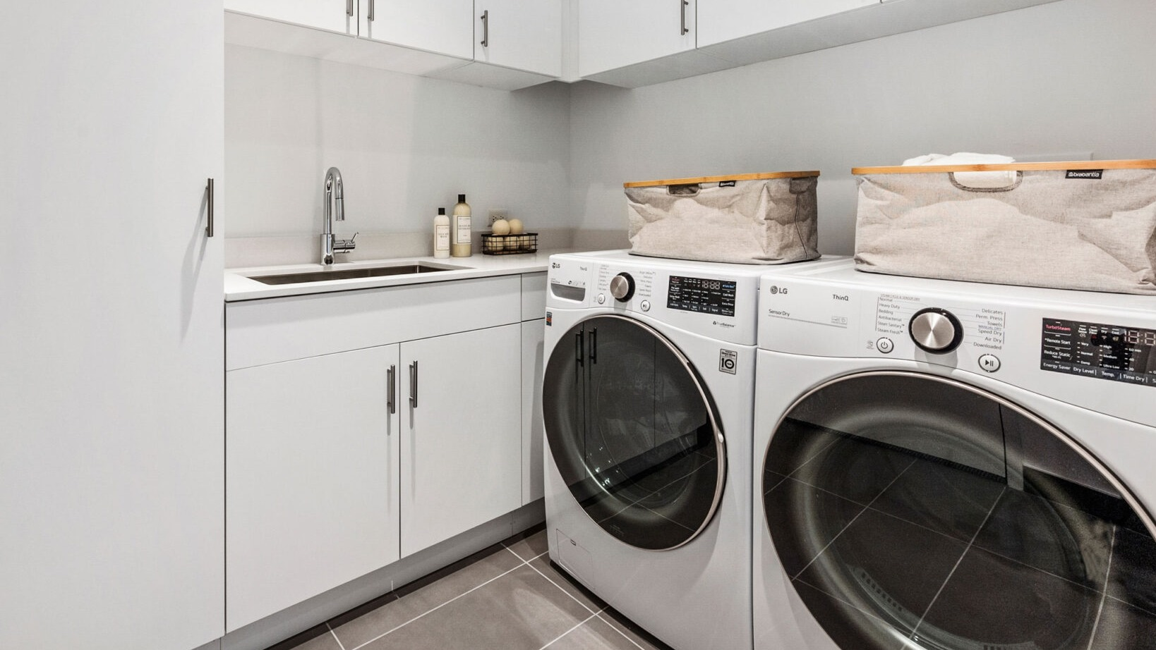 Modern in-unit laundry room with white cabinets, a sink, and front-loading washer and dryer at Parkline Chicago in Chicago