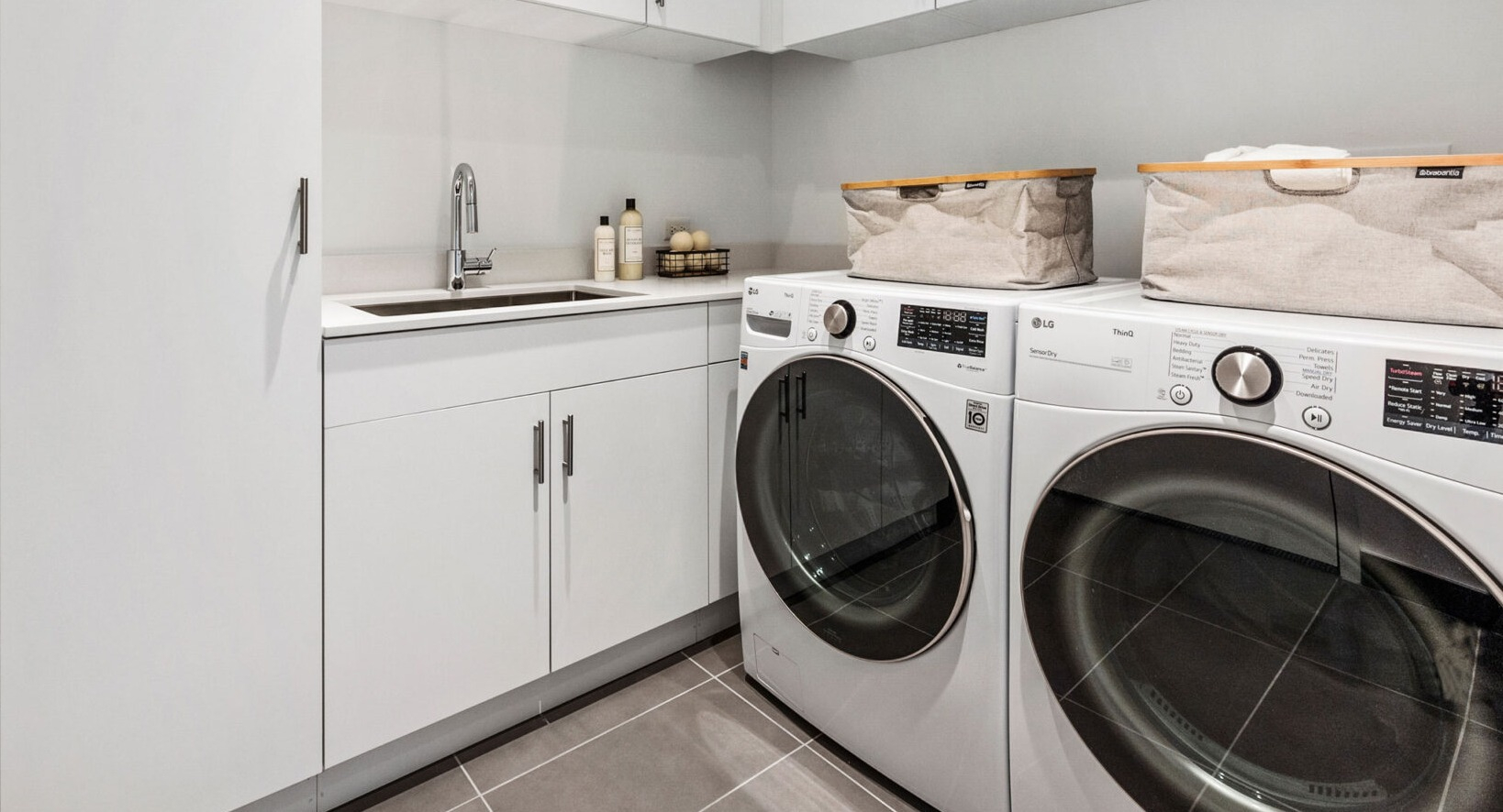 Modern in-unit laundry room with white cabinets, a sink, and front-loading washer and dryer at Parkline Chicago in Chicago