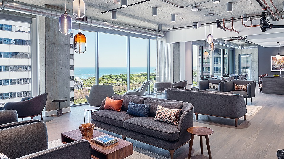 Inviting resident lounge area with multiple sofas, modern lighting, and large windows overlooking the city and lake at Parkline Chicago in Chicago