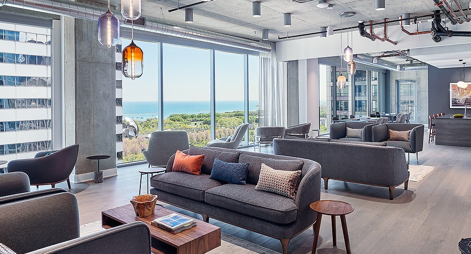 Inviting resident lounge area with multiple sofas, modern lighting, and large windows overlooking the city and lake at Parkline Chicago in Chicago