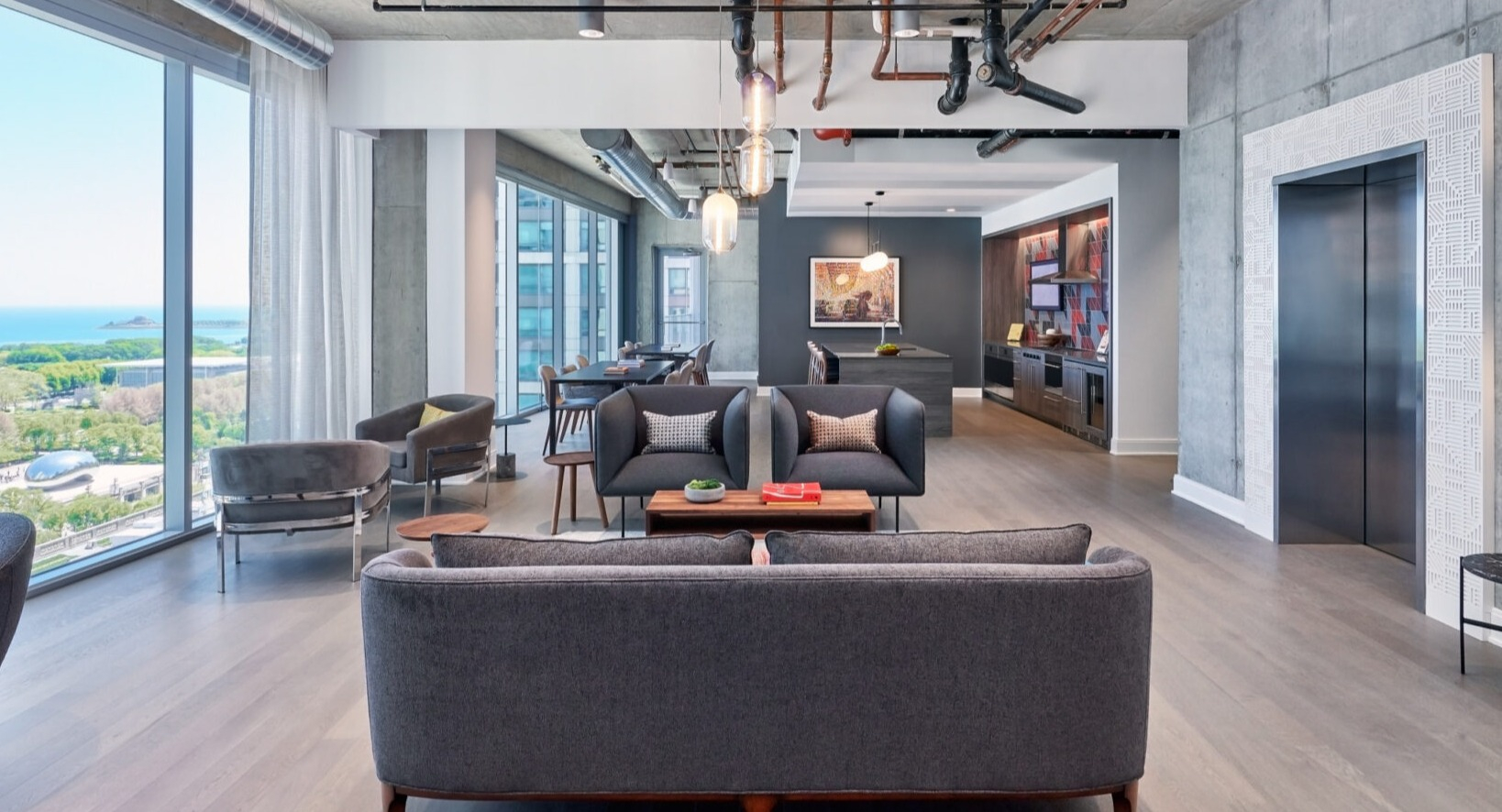 Expansive resident lounge with diverse seating, concrete accents, and floor-to-ceiling windows offering city and lake views at Parkline Chicago in Chicago