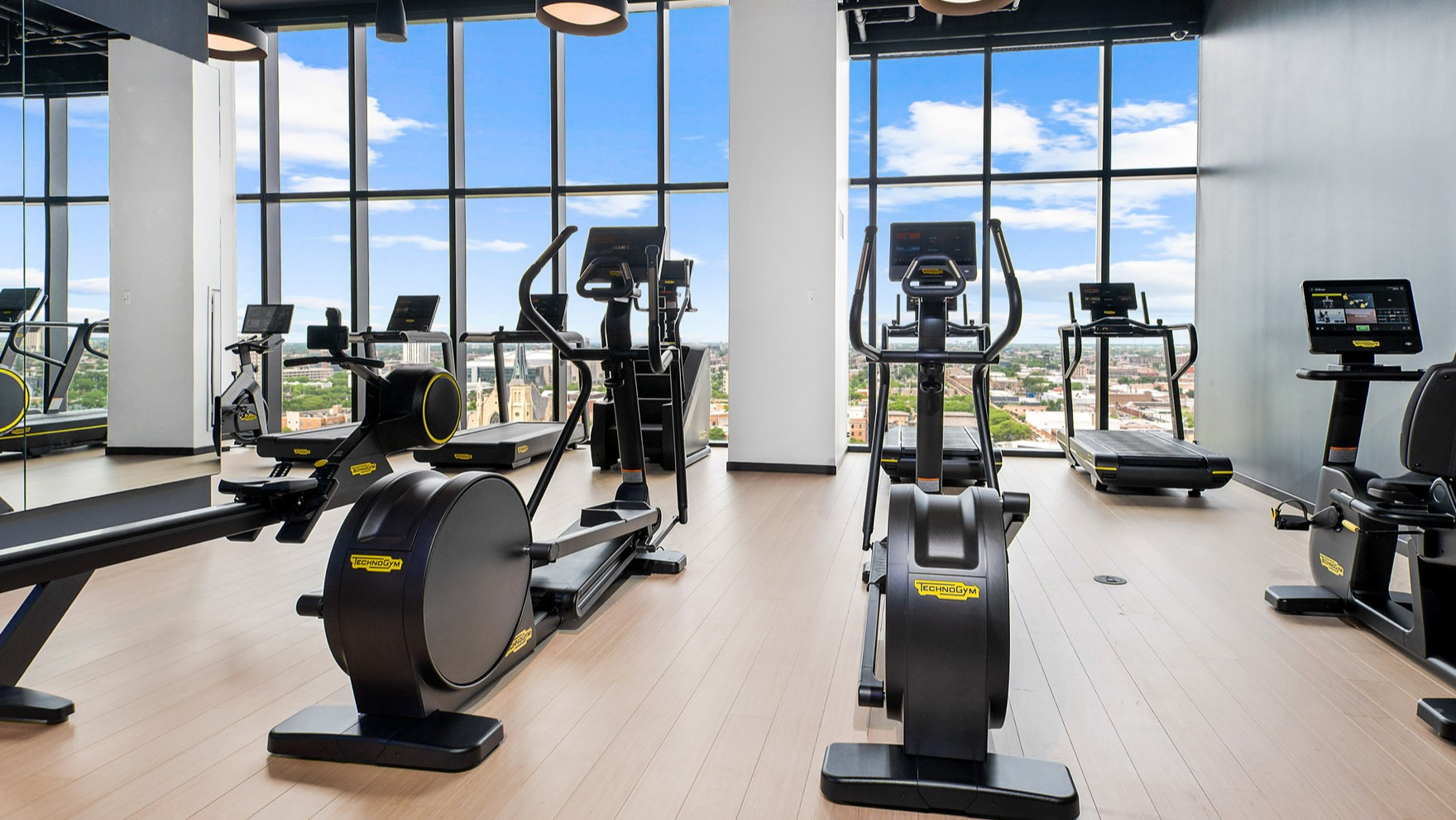 Modern fitness center at Parq Fulton in Chicago, featuring a variety of cardio machines and expansive city views through large windows