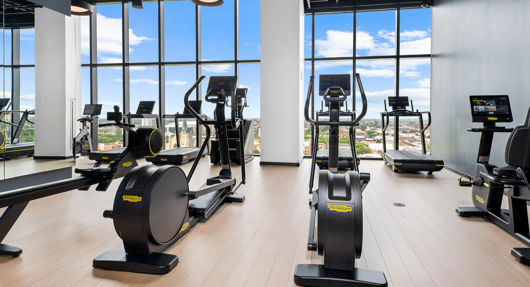 Modern fitness center at Parq Fulton in Chicago, featuring a variety of cardio machines and expansive city views through large windows