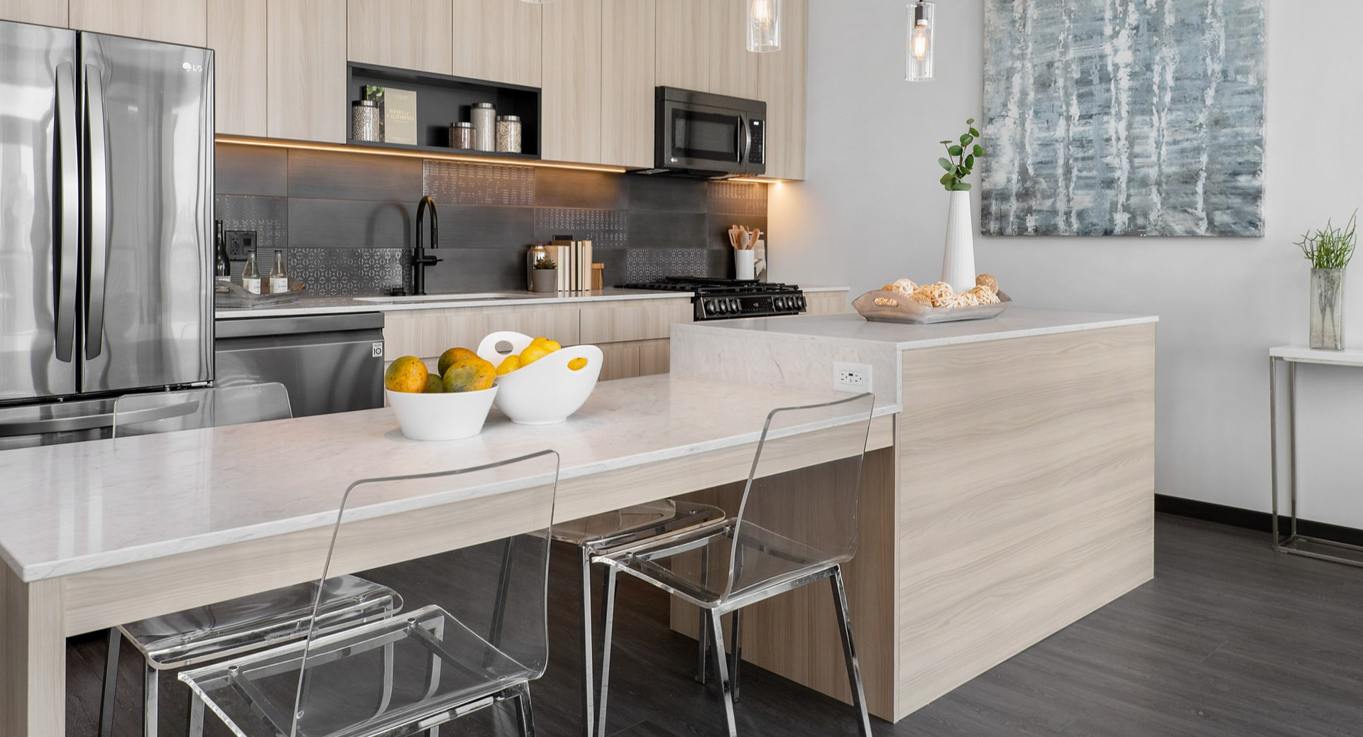 Modern apartment kitchen at Parq Fulton in Chicago, featuring light wood cabinets, a large island with seating, and stainless steel appliances