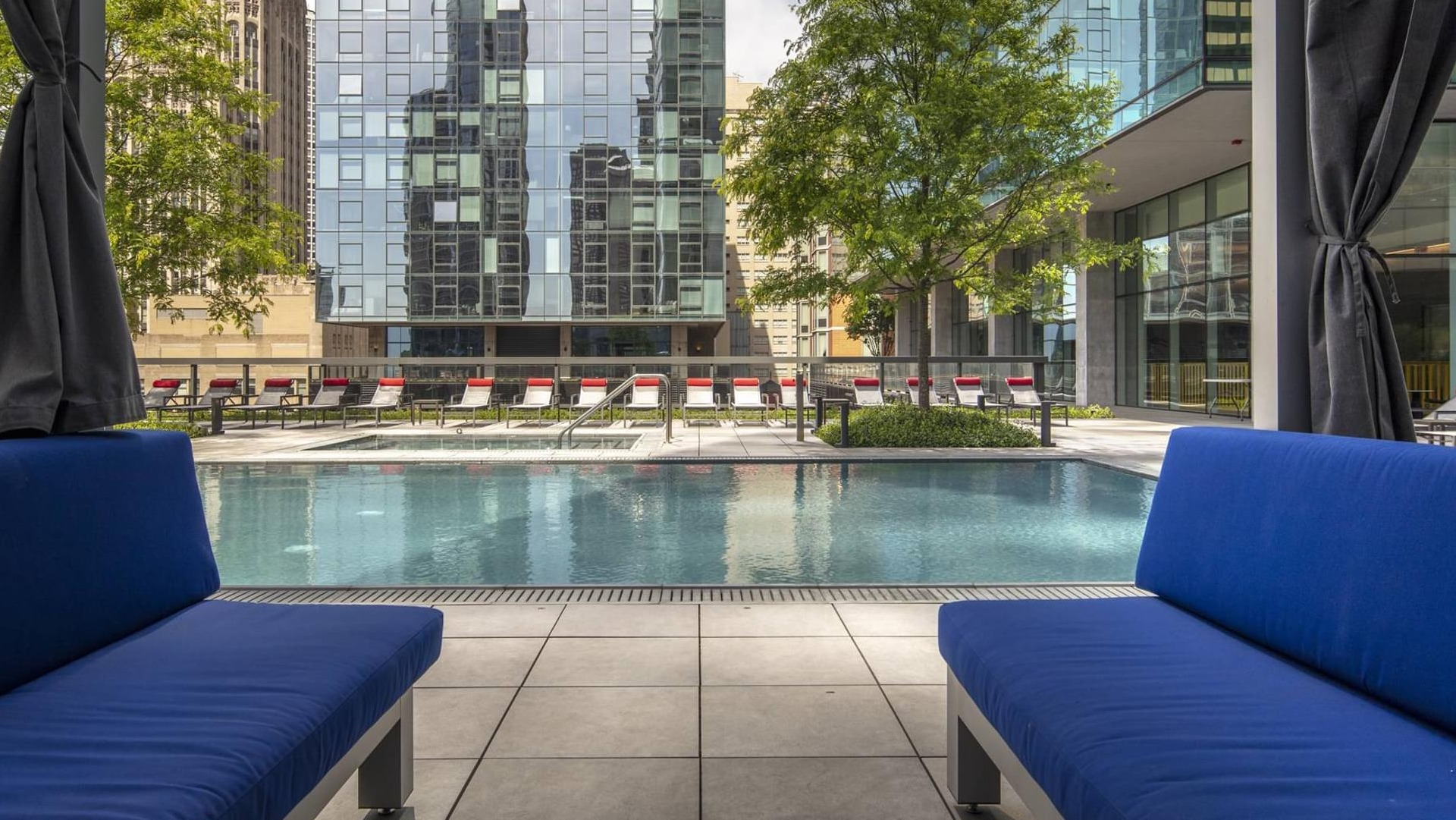 Poolside cabanas with cushioned seating facing a calm swimming pool and city high-rises at Optima Signature apartments in Chicago