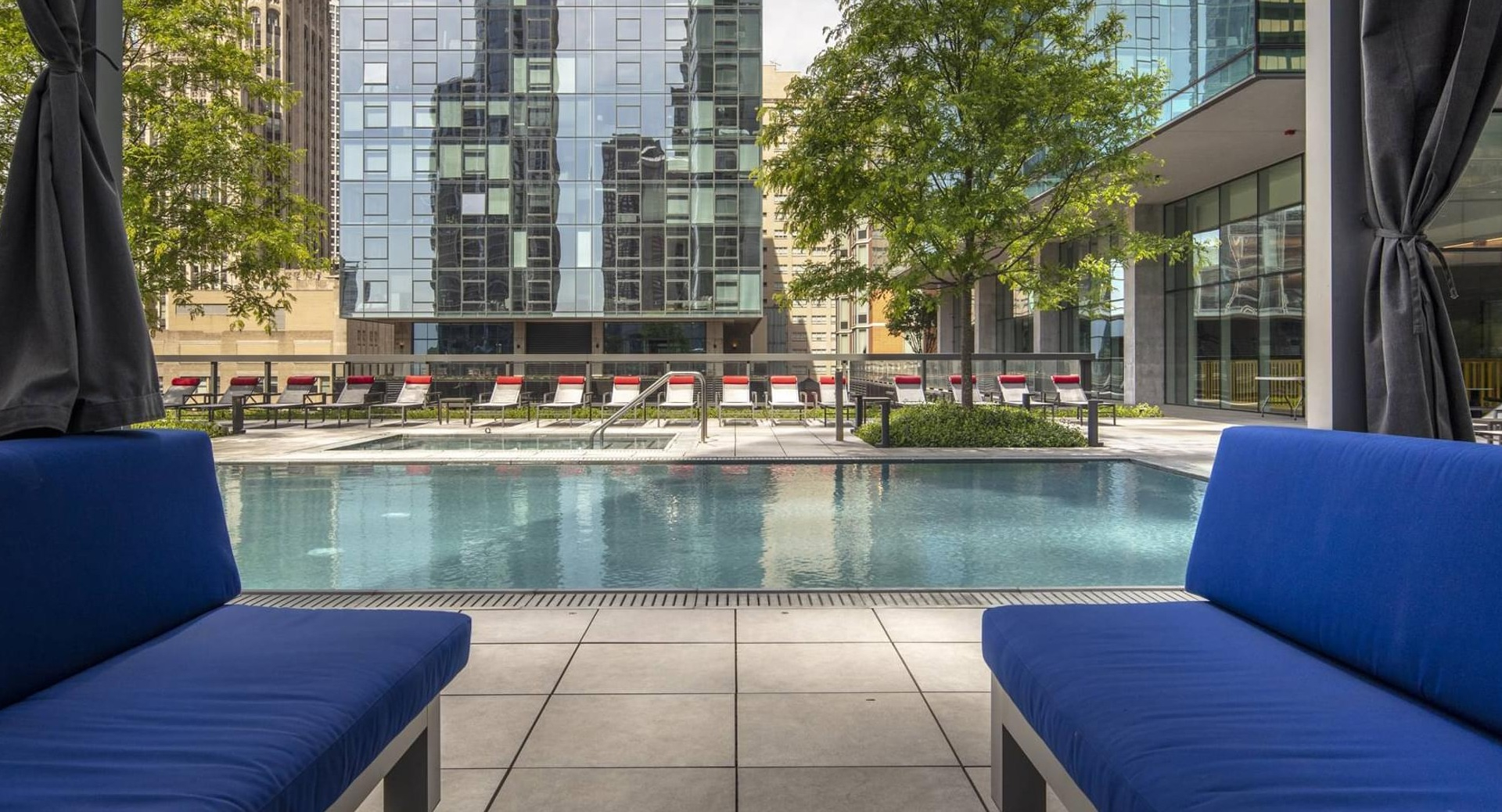 Poolside cabanas with cushioned seating facing a calm swimming pool and city high-rises at Optima Signature apartments in Chicago