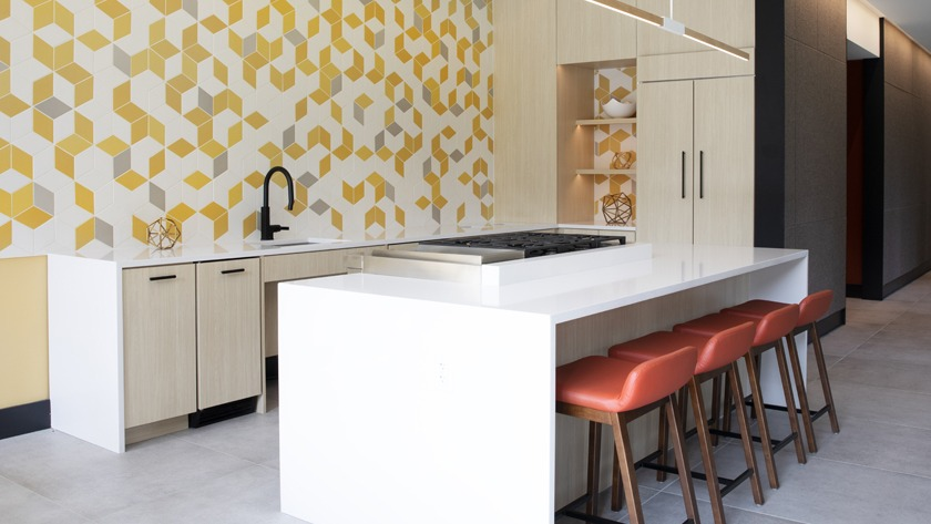 Vibrant clubroom kitchen at Porte Apartments Chicago, featuring a geometric yellow tile wall, a large island, and modern stools