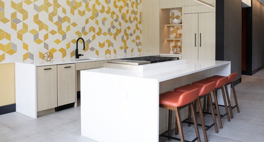 Vibrant clubroom kitchen at Porte Apartments Chicago, featuring a geometric yellow tile wall, a large island, and modern stools