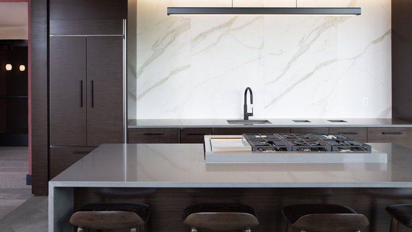 High-end gourmet kitchen in the clubroom at Porte Apartments Chicago, featuring a large island with a cooktop, and dark wood cabinetry