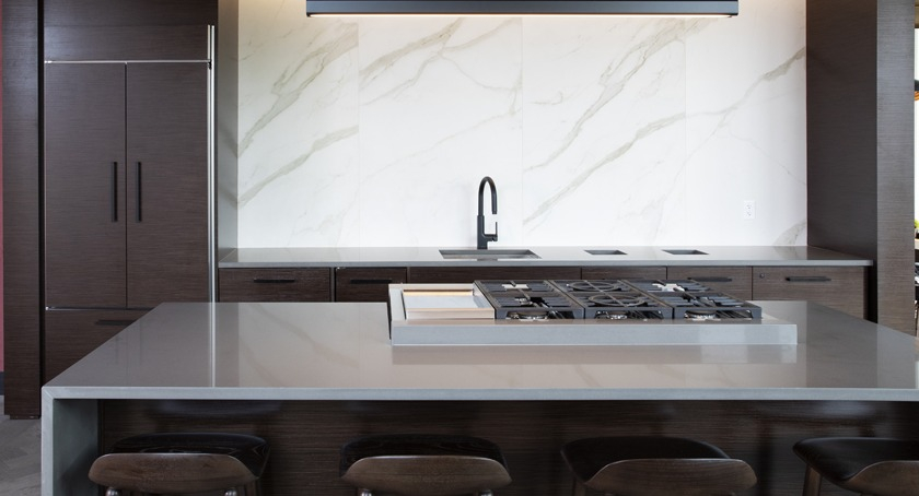 High-end gourmet kitchen in the clubroom at Porte Apartments Chicago, featuring a large island with a cooktop, and dark wood cabinetry