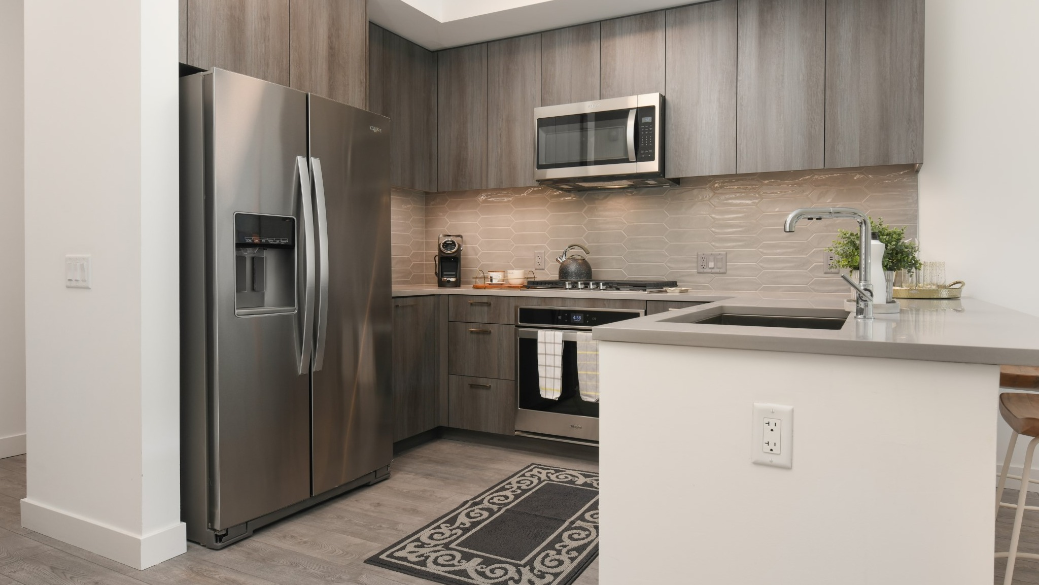 Modern apartment kitchen at Porte Apartments Chicago, featuring gray wood-grain cabinets, stainless steel appliances, and a breakfast bar