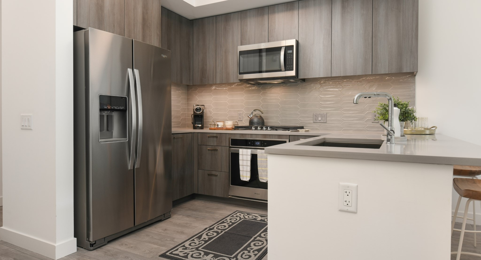 Modern apartment kitchen at Porte Apartments Chicago, featuring gray wood-grain cabinets, stainless steel appliances, and a breakfast bar