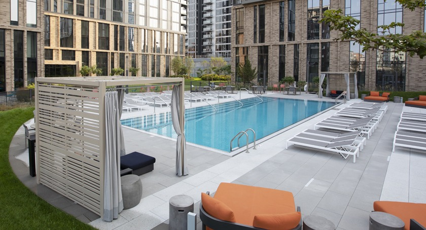 Scenic pool area at Porte Apartments Chicago, featuring comfortable lounge chairs, private cabanas, and a surrounding green lawn