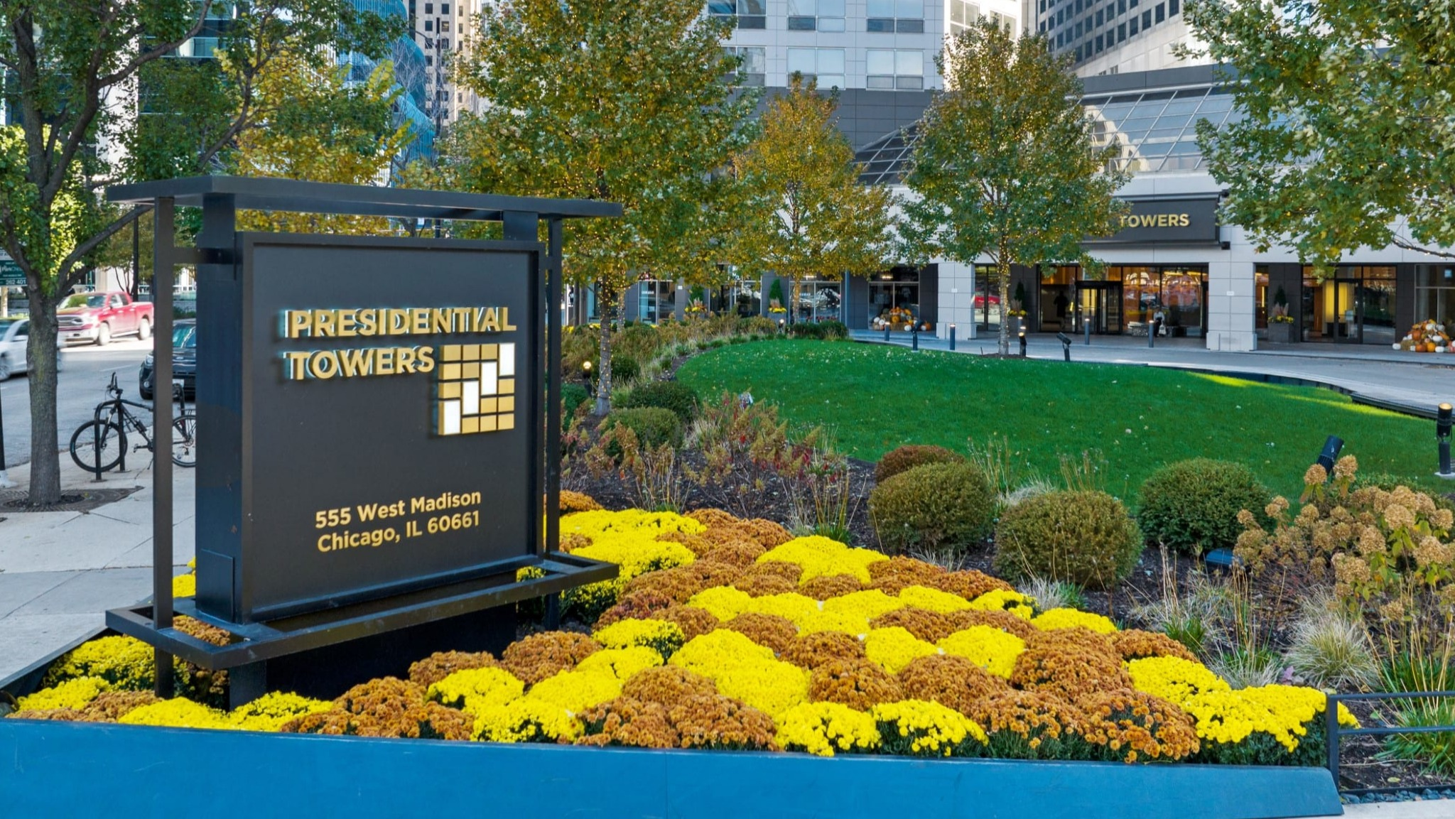 Community entrance at Presidential Towers in Chicago with landscaped flower beds, clear property signage, and a high-rise backdrop on West Madison