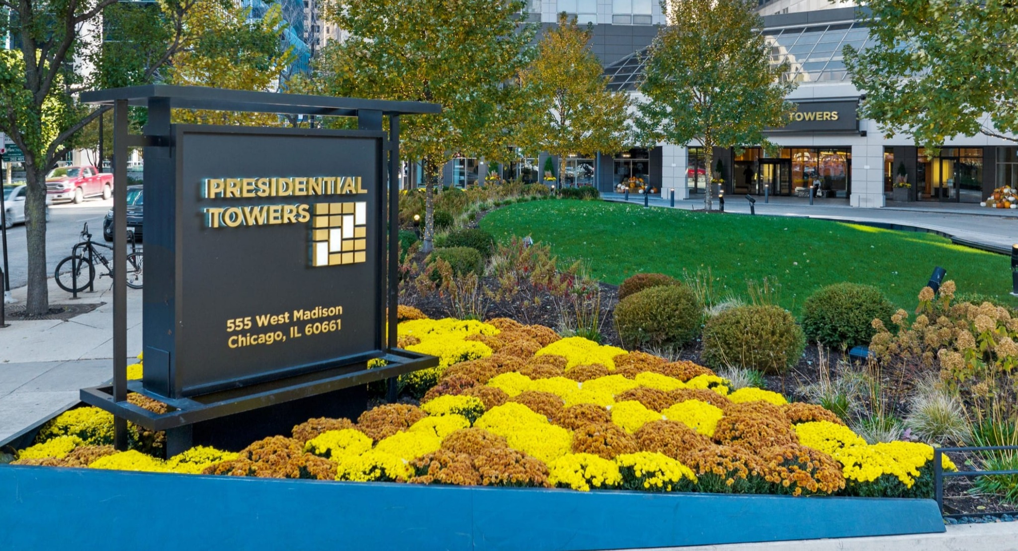 Community entrance at Presidential Towers in Chicago with landscaped flower beds, clear property signage, and a high-rise backdrop on West Madison