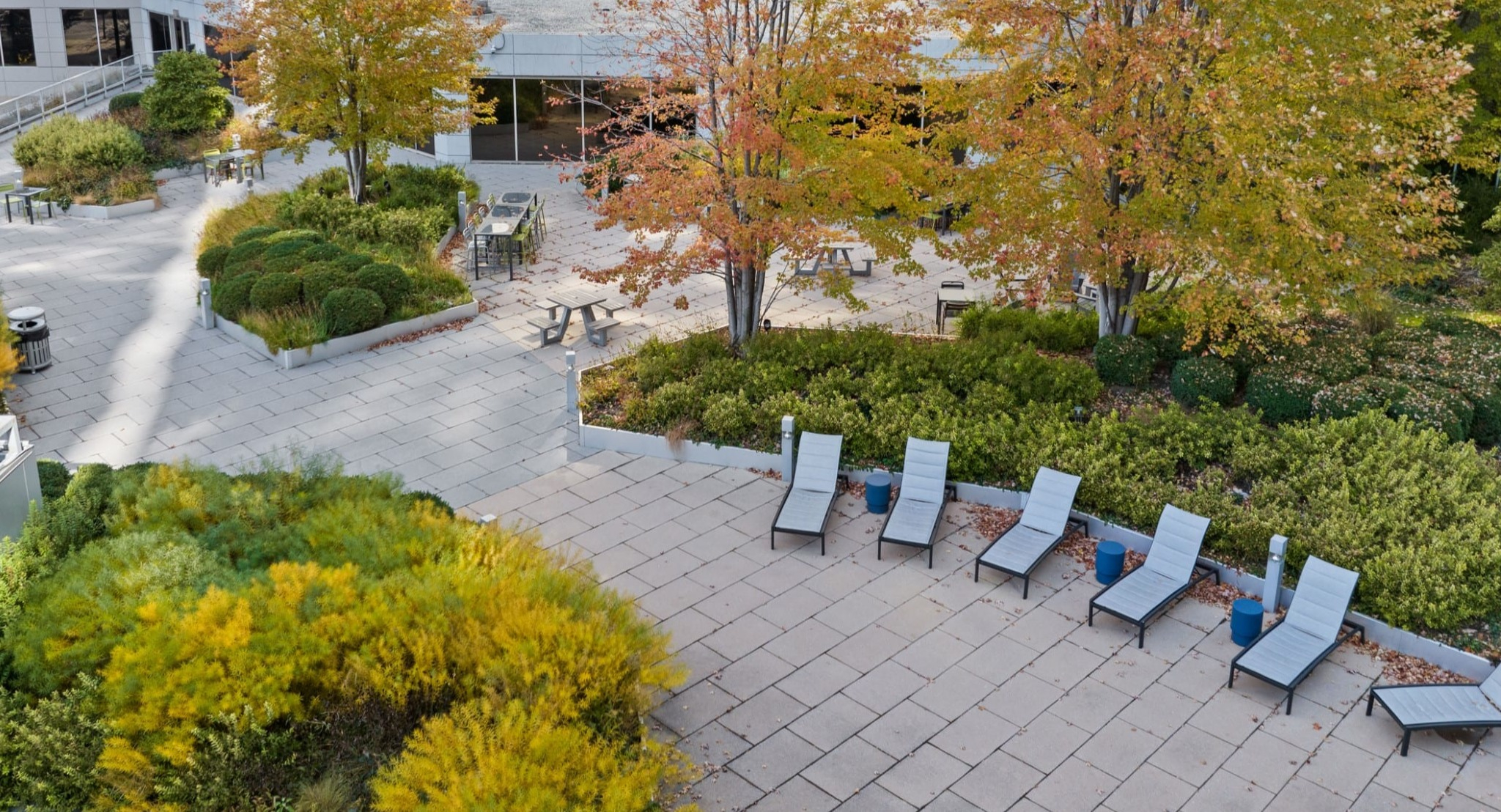 Expansive landscaped courtyard at Presidential Towers Chicago featuring trees, greenery, paved paths, picnic tables, and sun-lounger chairs for relaxing