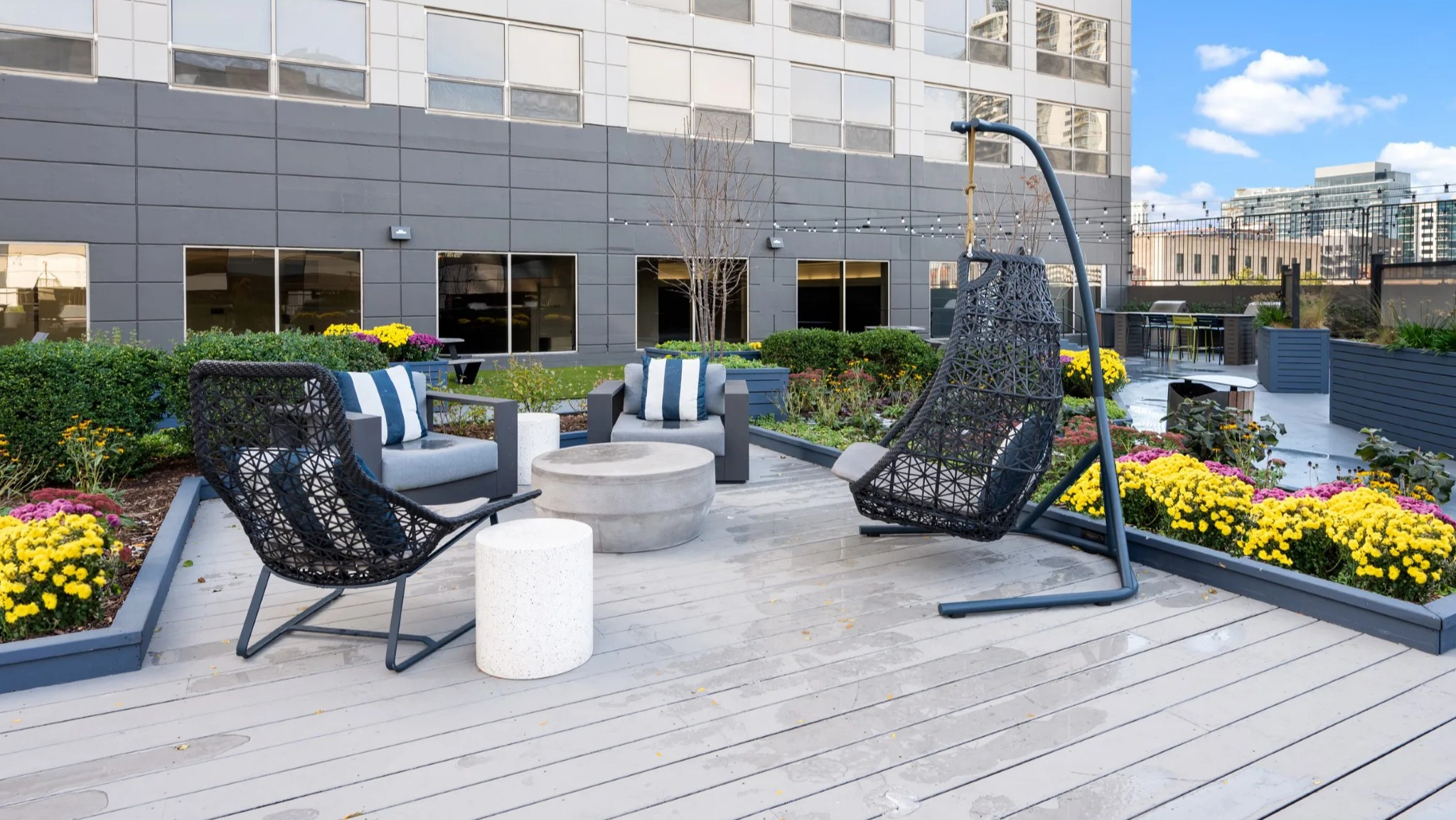 Rooftop lounge at Presidential Towers Chicago with hanging chairs, cushioned seating, string lights, and a circular fire pit amid colorful planters