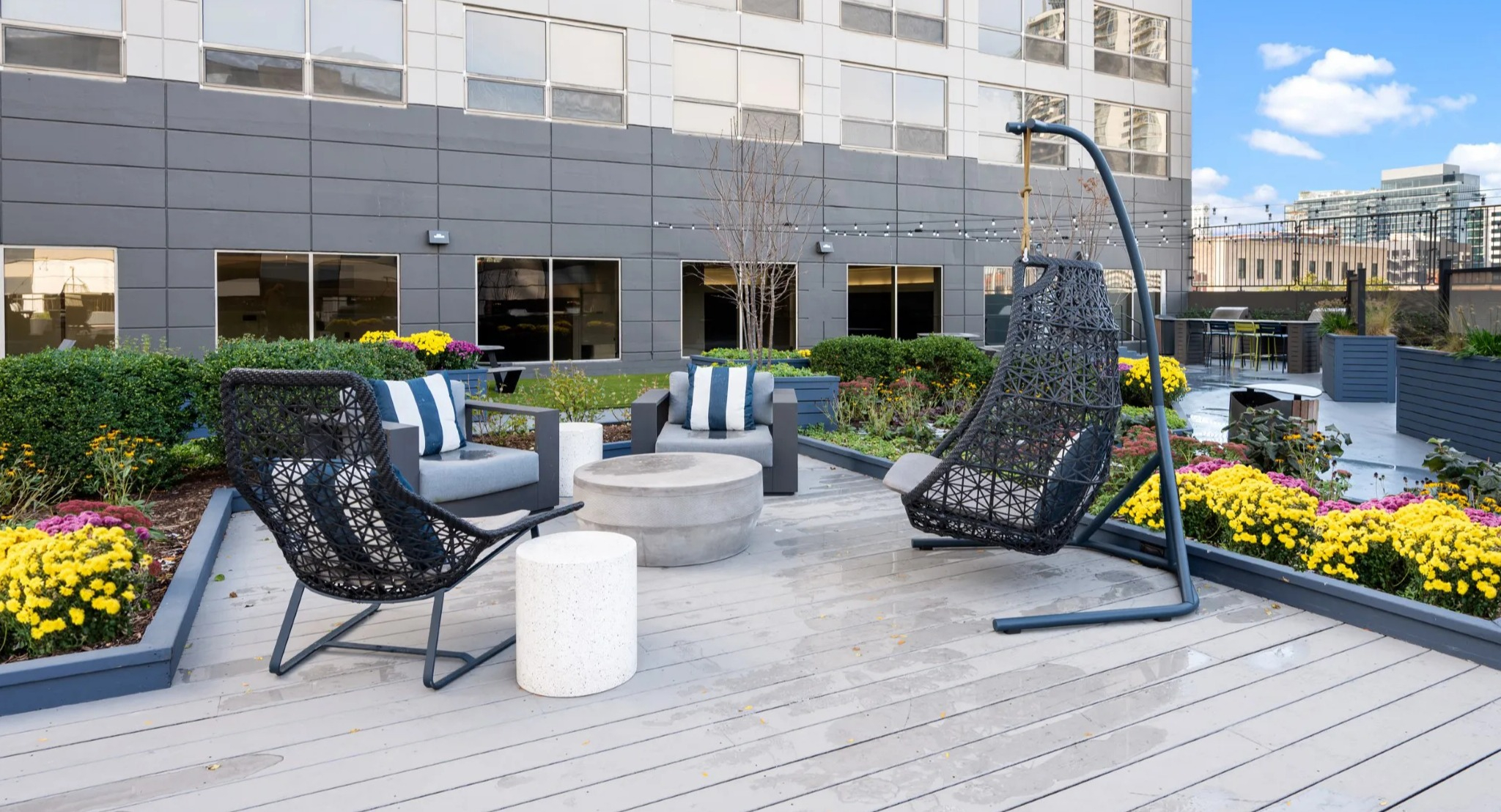 Rooftop lounge at Presidential Towers Chicago with hanging chairs, cushioned seating, string lights, and a circular fire pit amid colorful planters