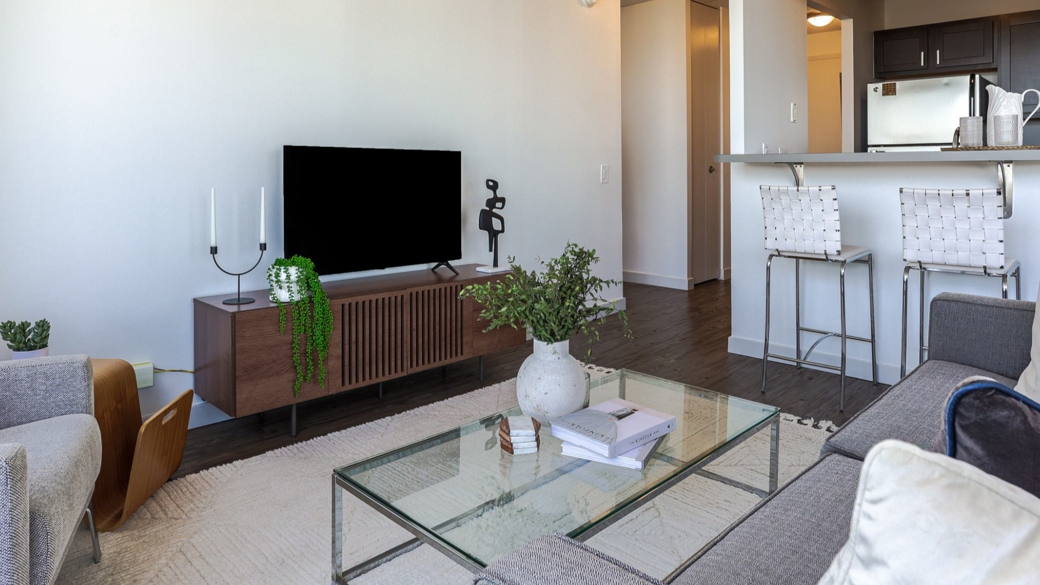 Modern living area at Presidential Towers in Chicago showing TV console, seating, and a breakfast bar leading to the kitchen with stainless appliances