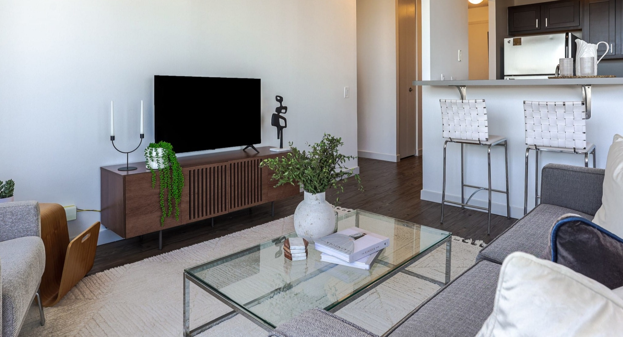 Modern living area at Presidential Towers in Chicago showing TV console, seating, and a breakfast bar leading to the kitchen with stainless appliances