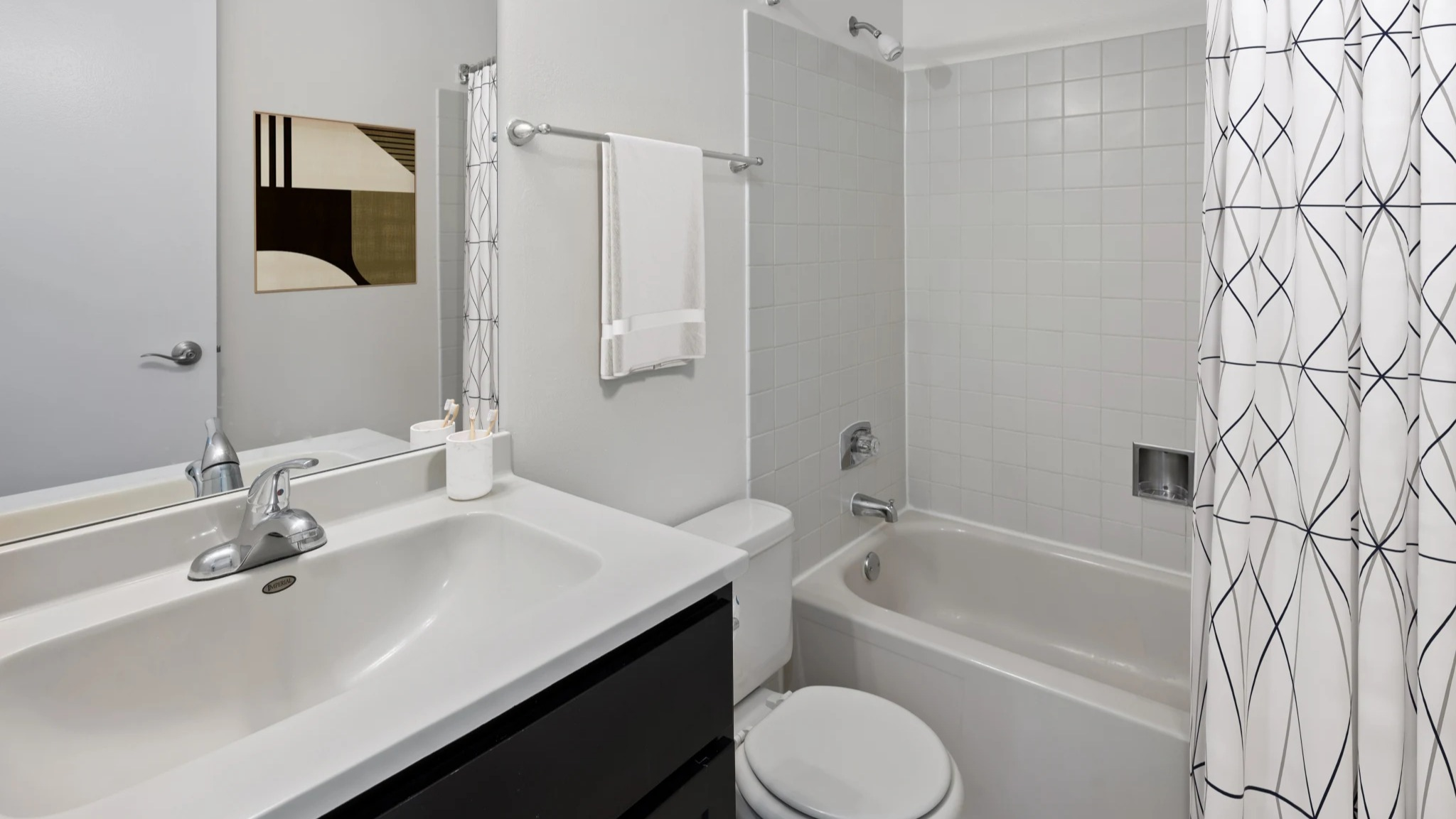 Bright modern bathroom at Presidential Towers in Chicago featuring a tub-shower combo, large vanity mirror, white tile, and sleek fixtures