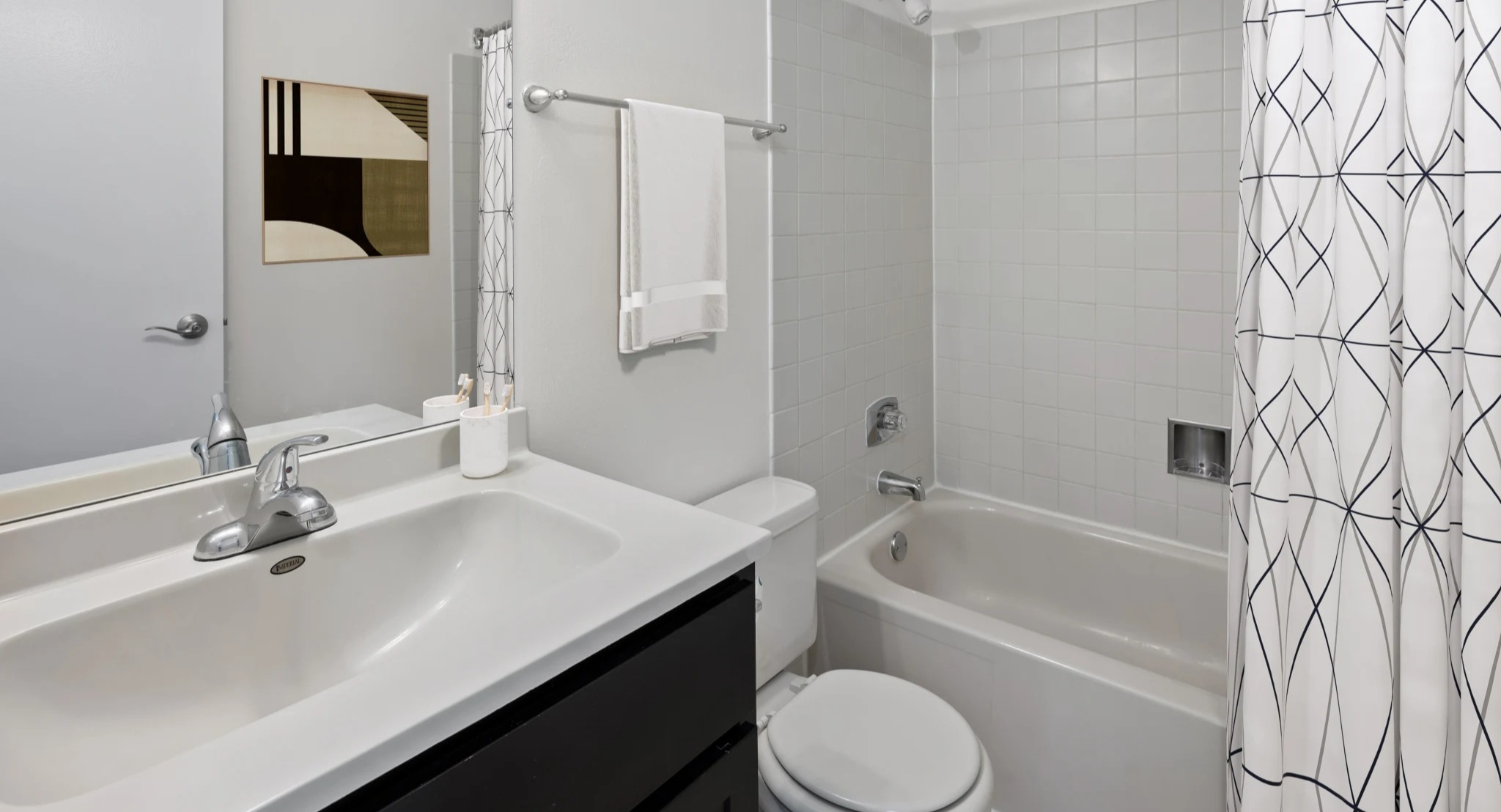 Bright modern bathroom at Presidential Towers in Chicago featuring a tub-shower combo, large vanity mirror, white tile, and sleek fixtures