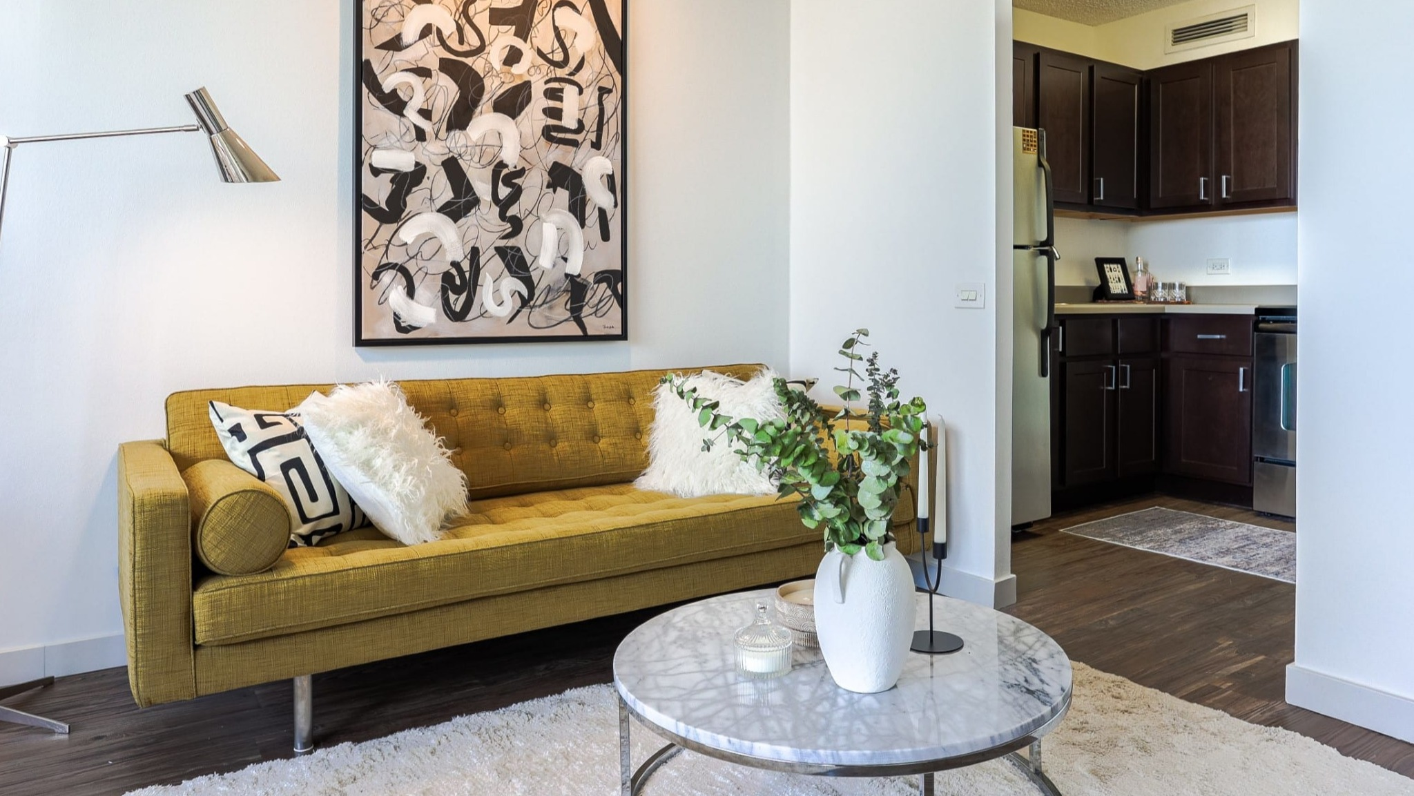 Contemporary living space at Presidential Towers in Chicago with mustard sofa, art wall, floor lamp, and open doorway to the updated kitchen